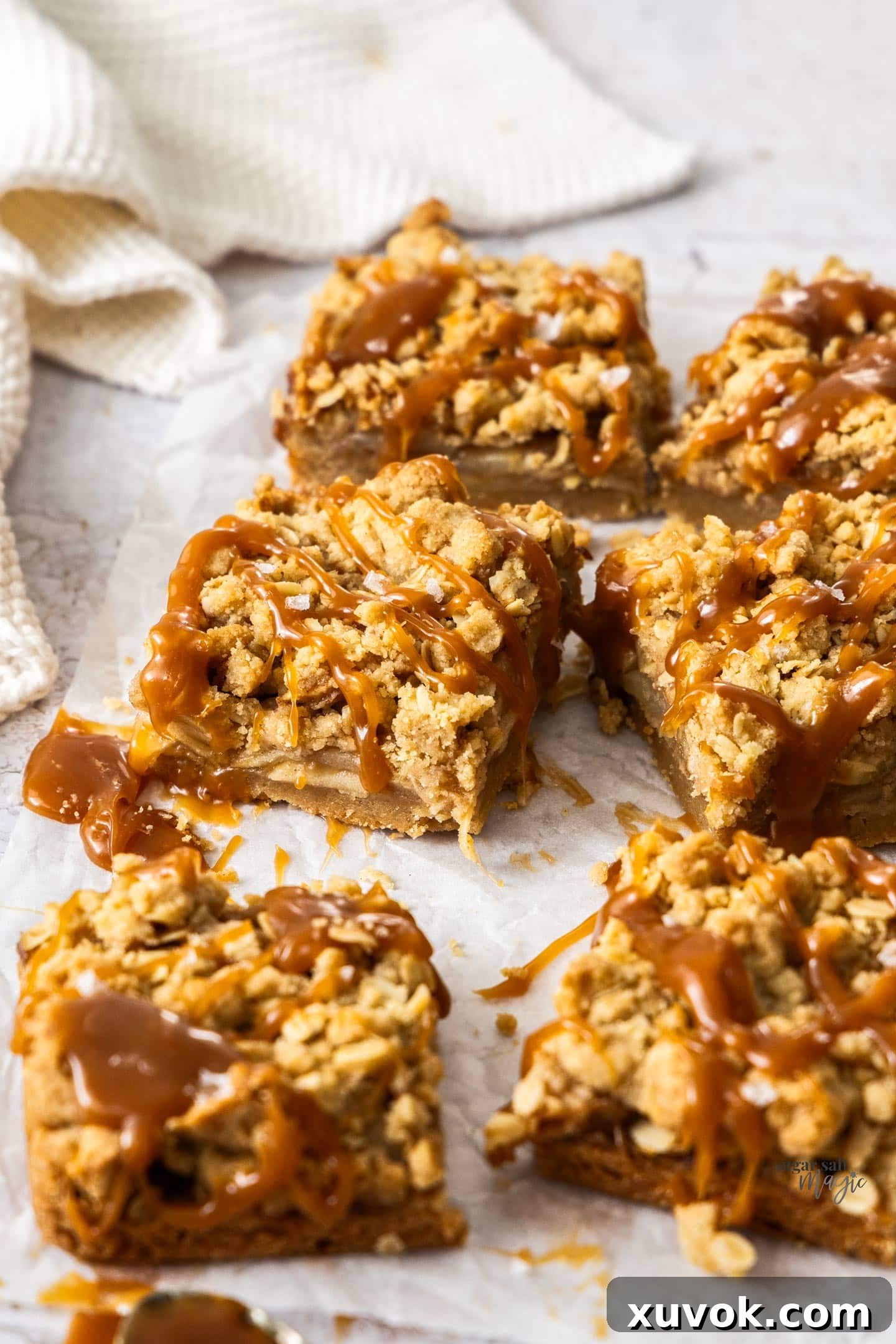 Six perfectly baked Salted Caramel Apple Pie Bars displayed on a sheet of baking paper, ready to be enjoyed.