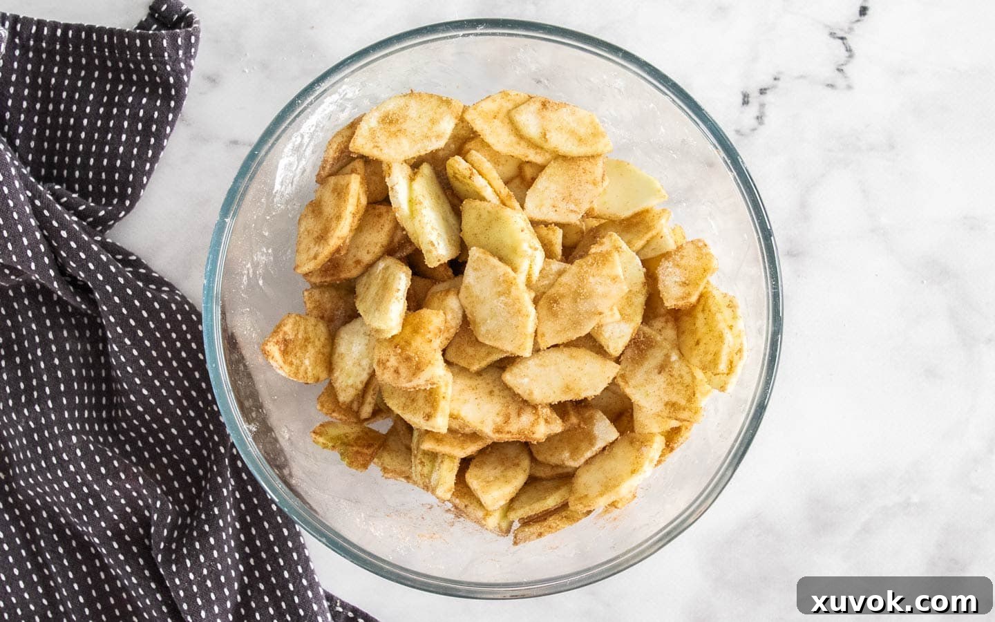 Thinly sliced apples in a bowl, generously coated with sugar and warm spices for the filling.