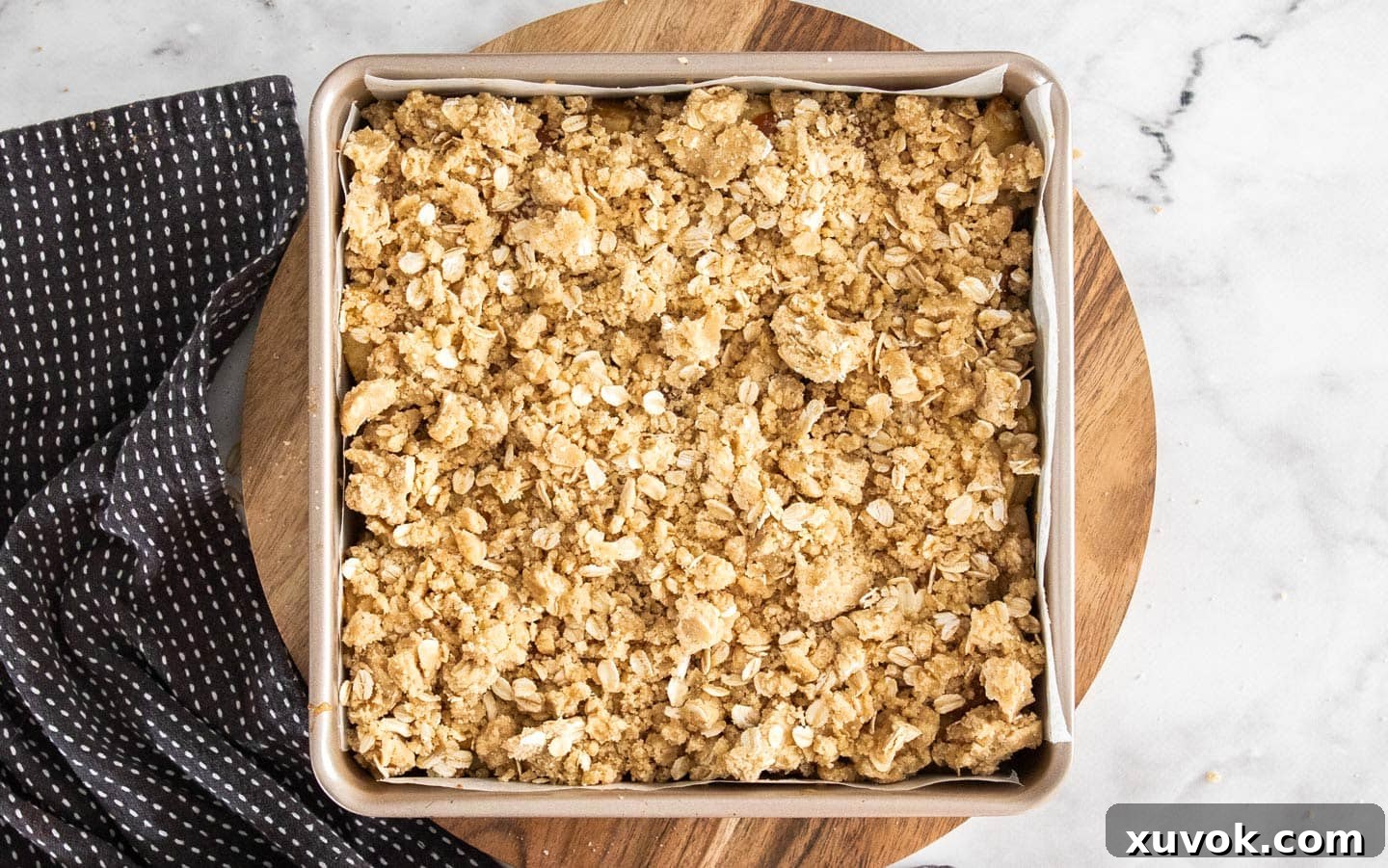 The oat crumble topping generously scattered over the apples and caramel in the baking pan, ready for the final bake.