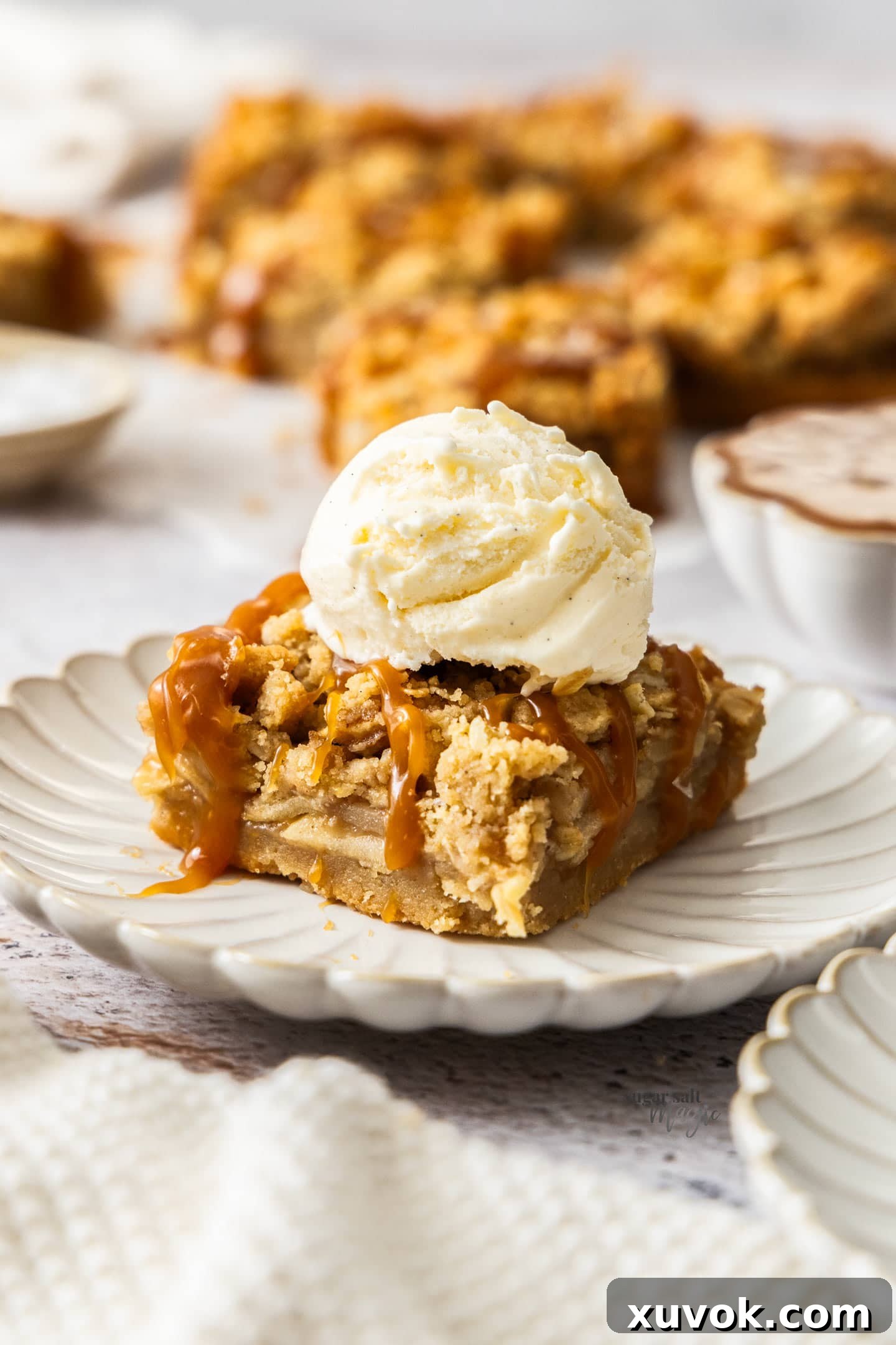 A single square salted caramel apple pie bar on a dessert plate, topped with a scoop of vanilla ice cream.
