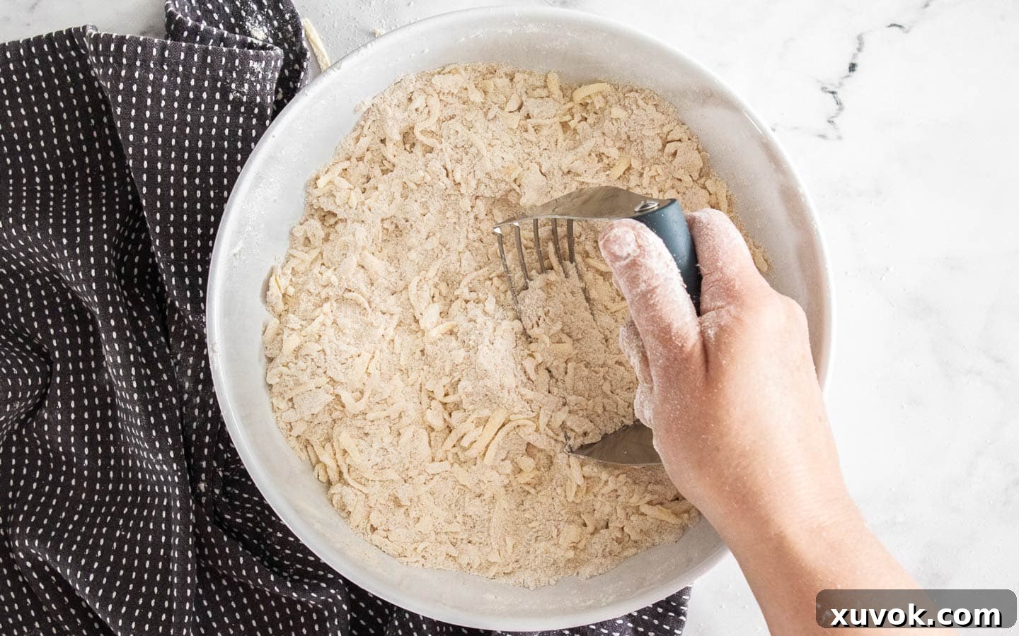 A pastry blender being used to incorporate cold butter into the dry ingredients for the shortbread dough.