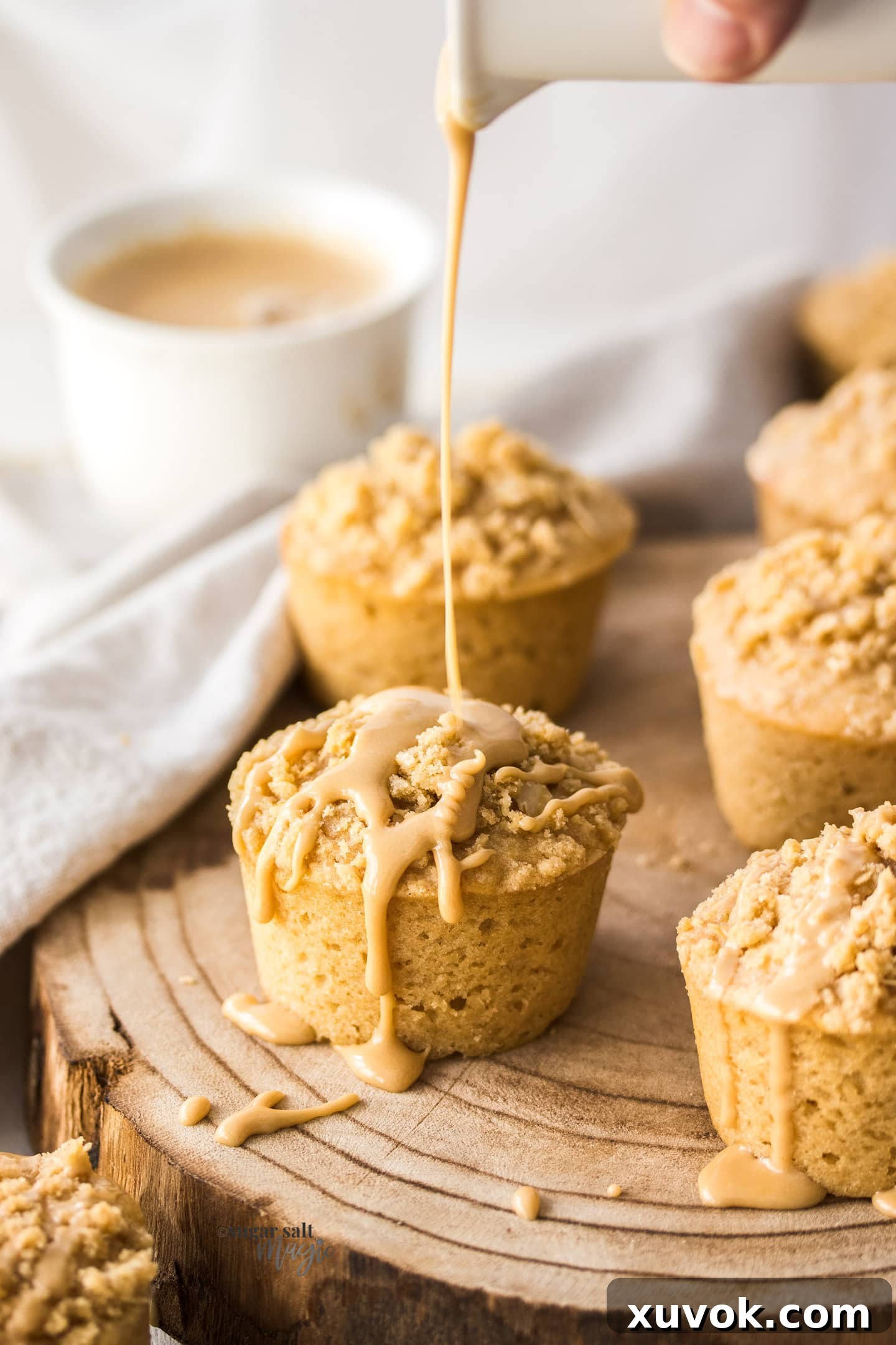 Coffee glaze being poured over the top of a muffin on a wooden board.