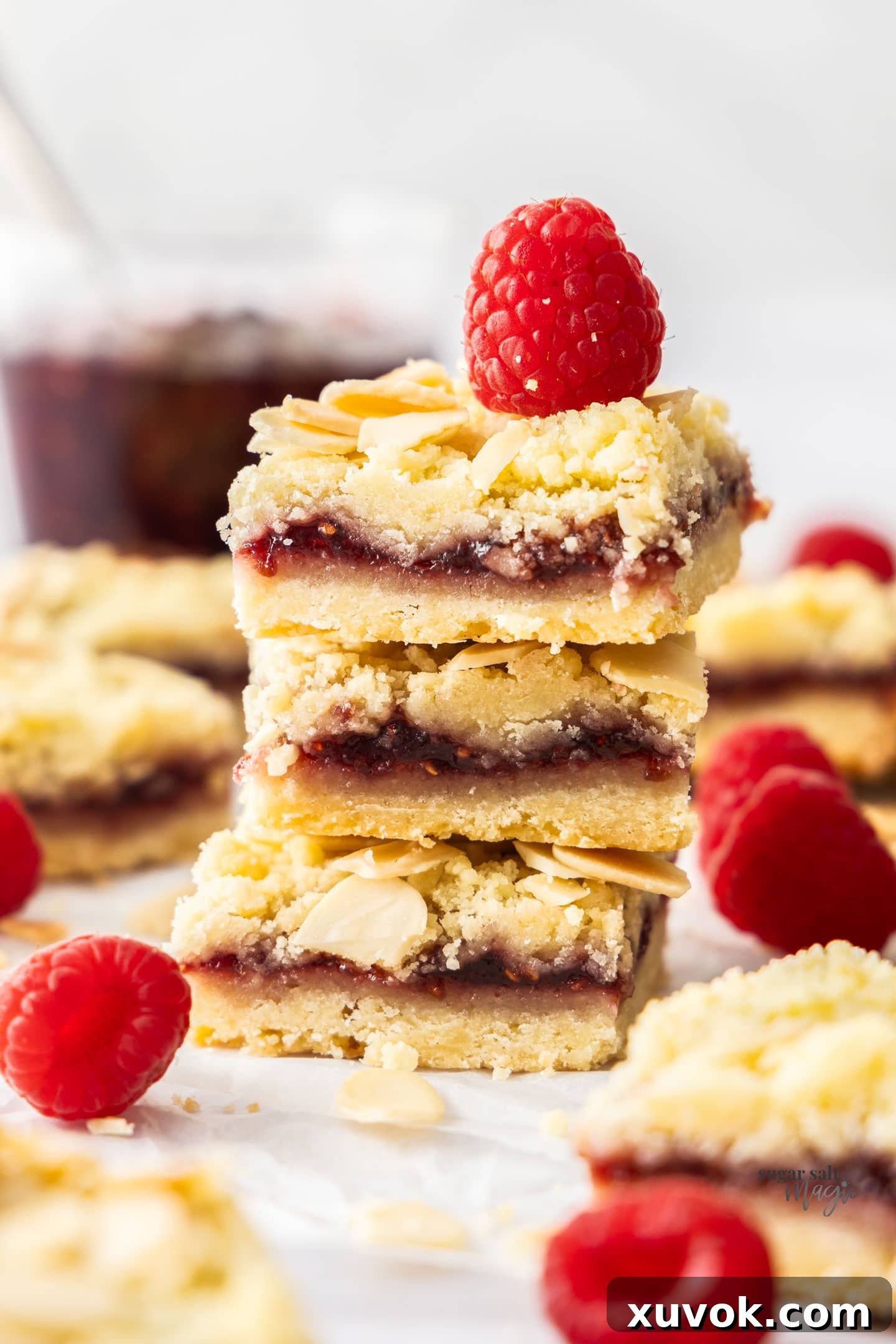 A stack of 3 raspberry shortbread bars, showcasing their golden crust and red jam filling.
