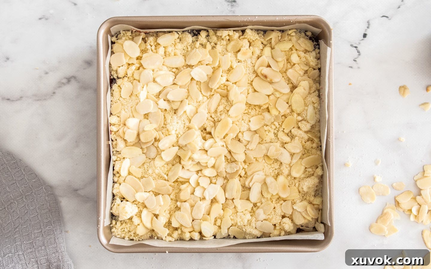 The shortbread topping and almonds scattered on top of the jam layer, ready for the final bake.