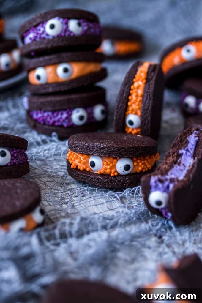 Piles of chocolate sandwich cookies decorated with eye balls to look like cute little monsters. The cookies are on a white plate with Halloween themed sprinkles.