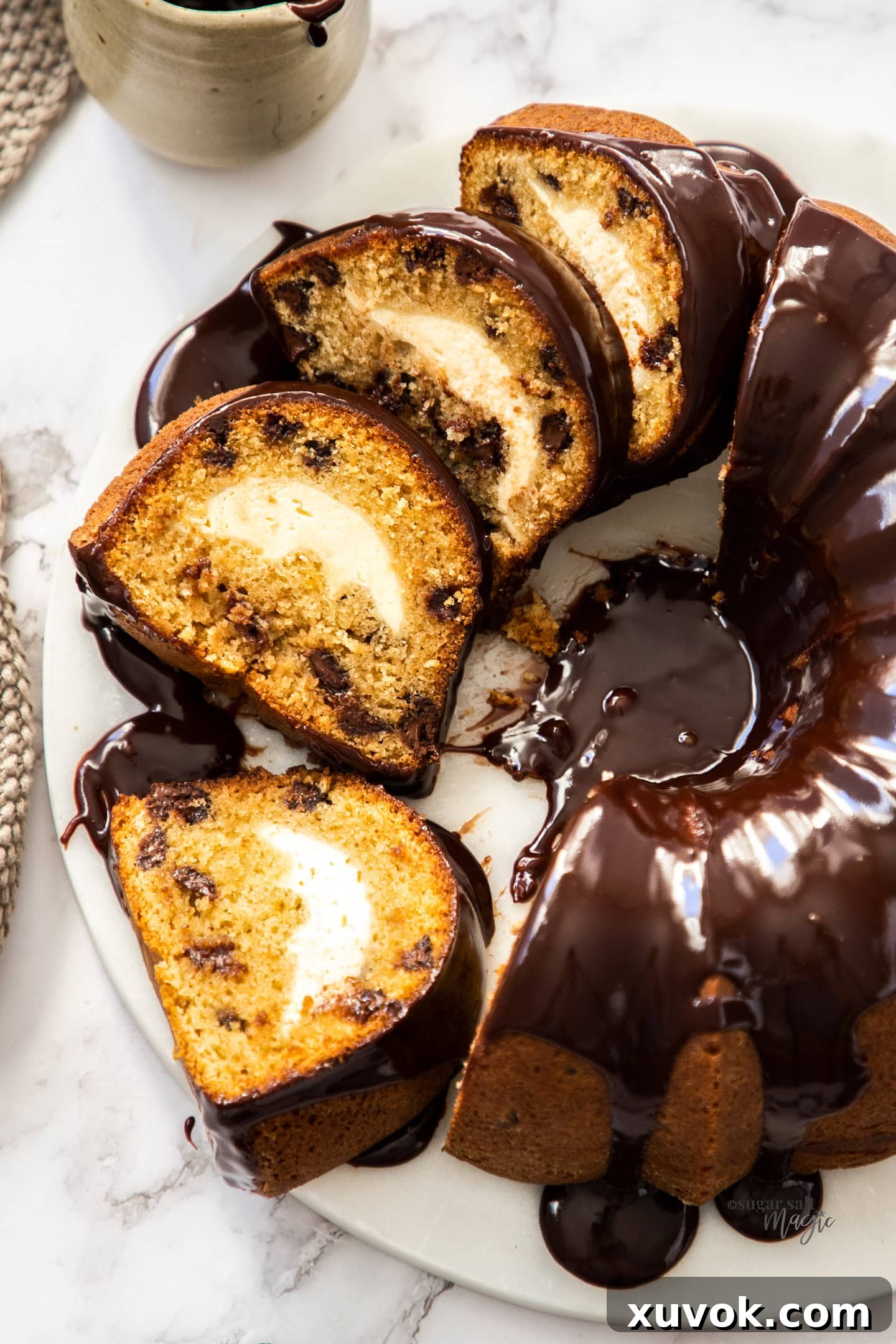 Top down view of a sliced bundt cake topped with chocolate ganache on a marble platter.