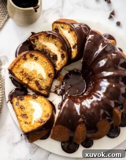 A sliced bundt cake topped with chocolate ganache on a marble platter.