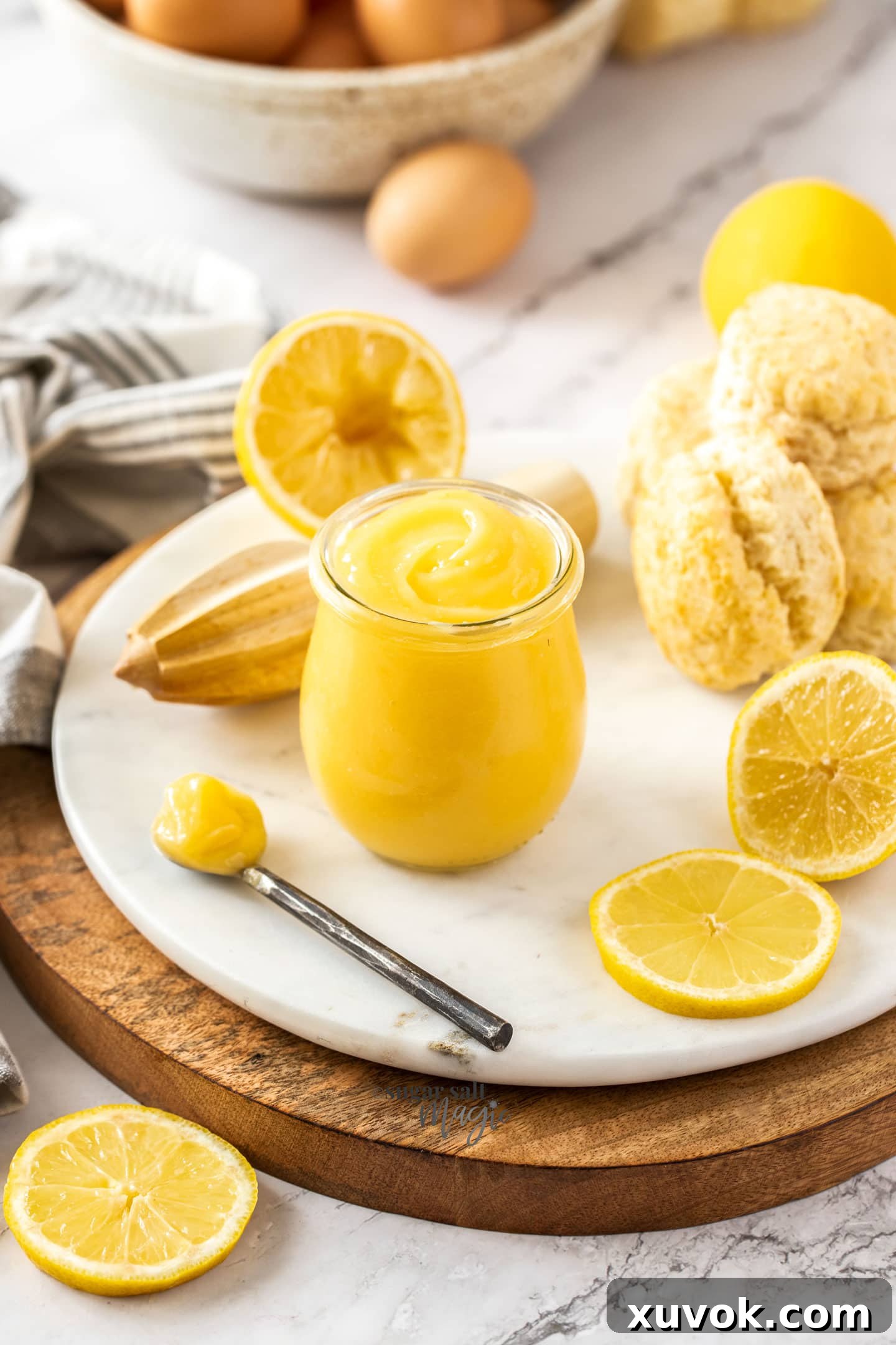 A glass jar of lemon curd on a white platter with scones sitting next to it.