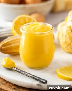 A glass jar filled with lemon curd with a spoon sitting next to it.