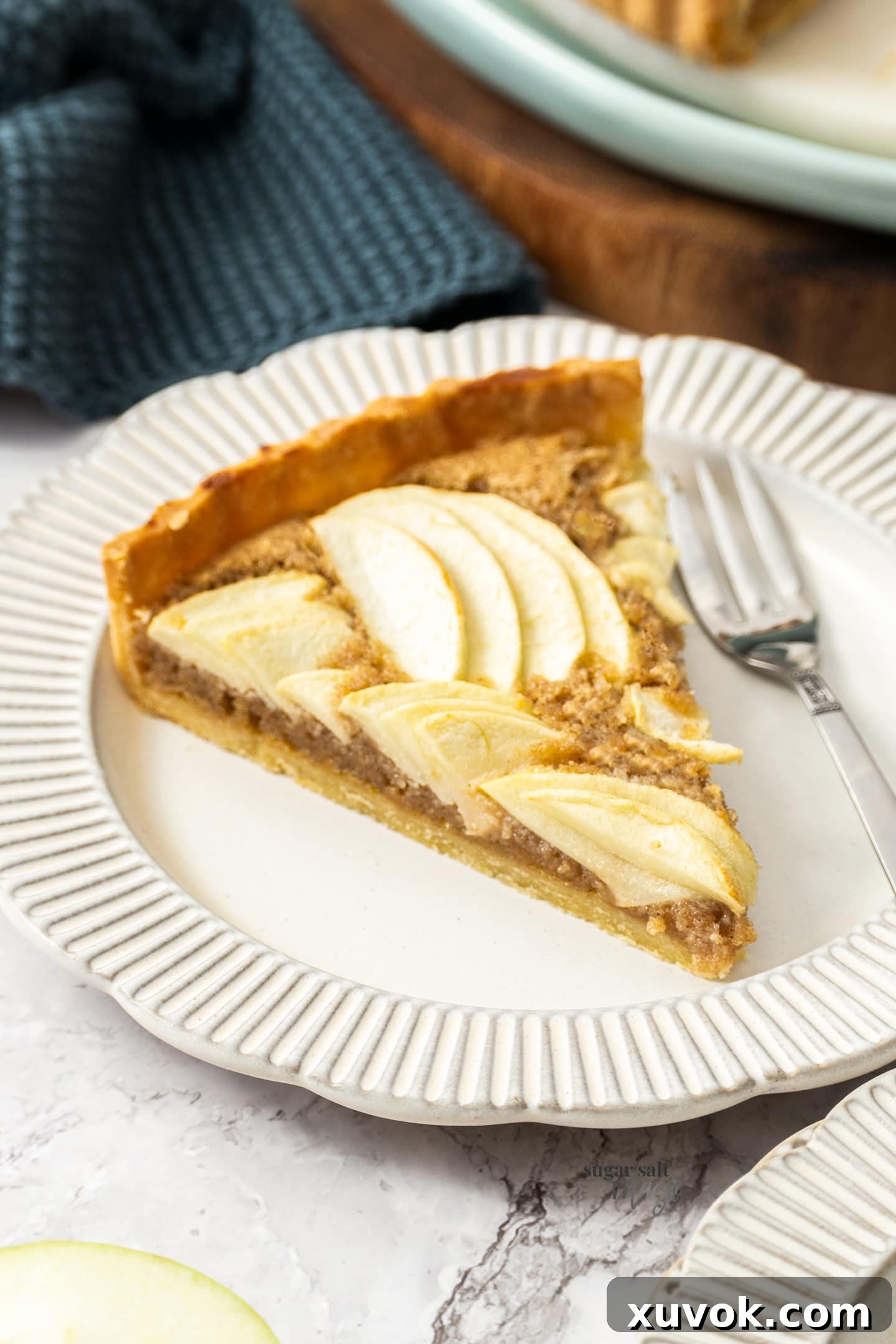 A perfectly sliced portion of apple frangipane tart, ready to be enjoyed on a small dessert plate.