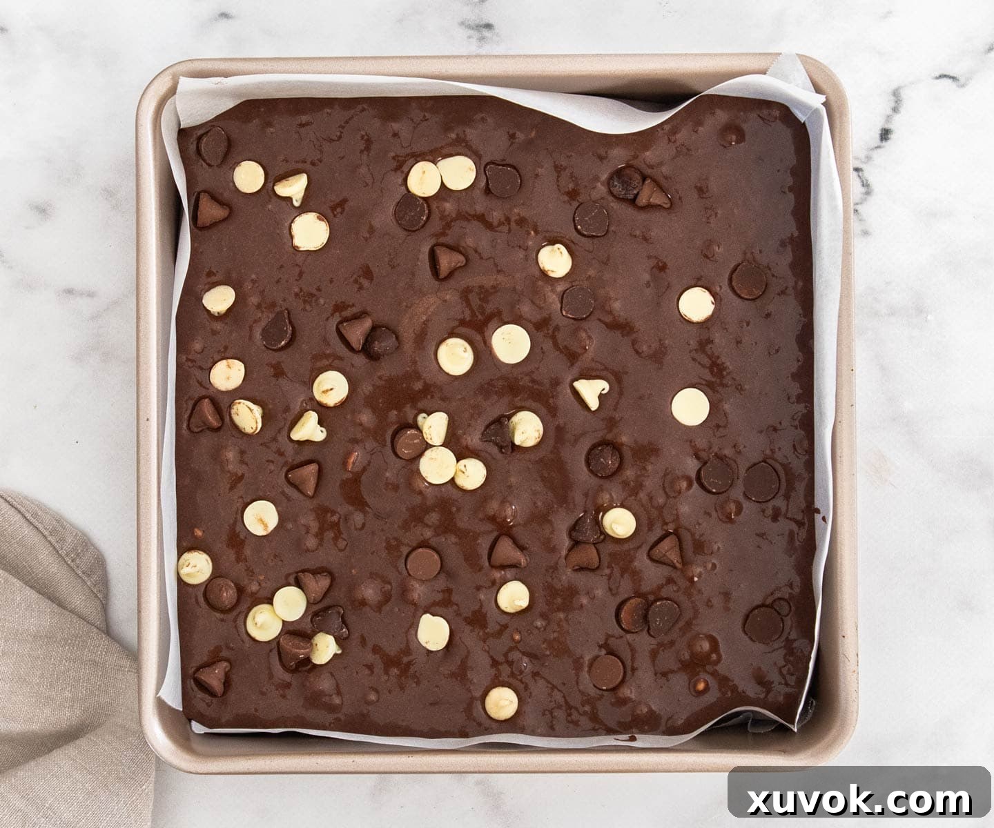 The raw brownie batter in a square baking pan, topped with a generous sprinkle of mixed chocolate chips, ready for baking.