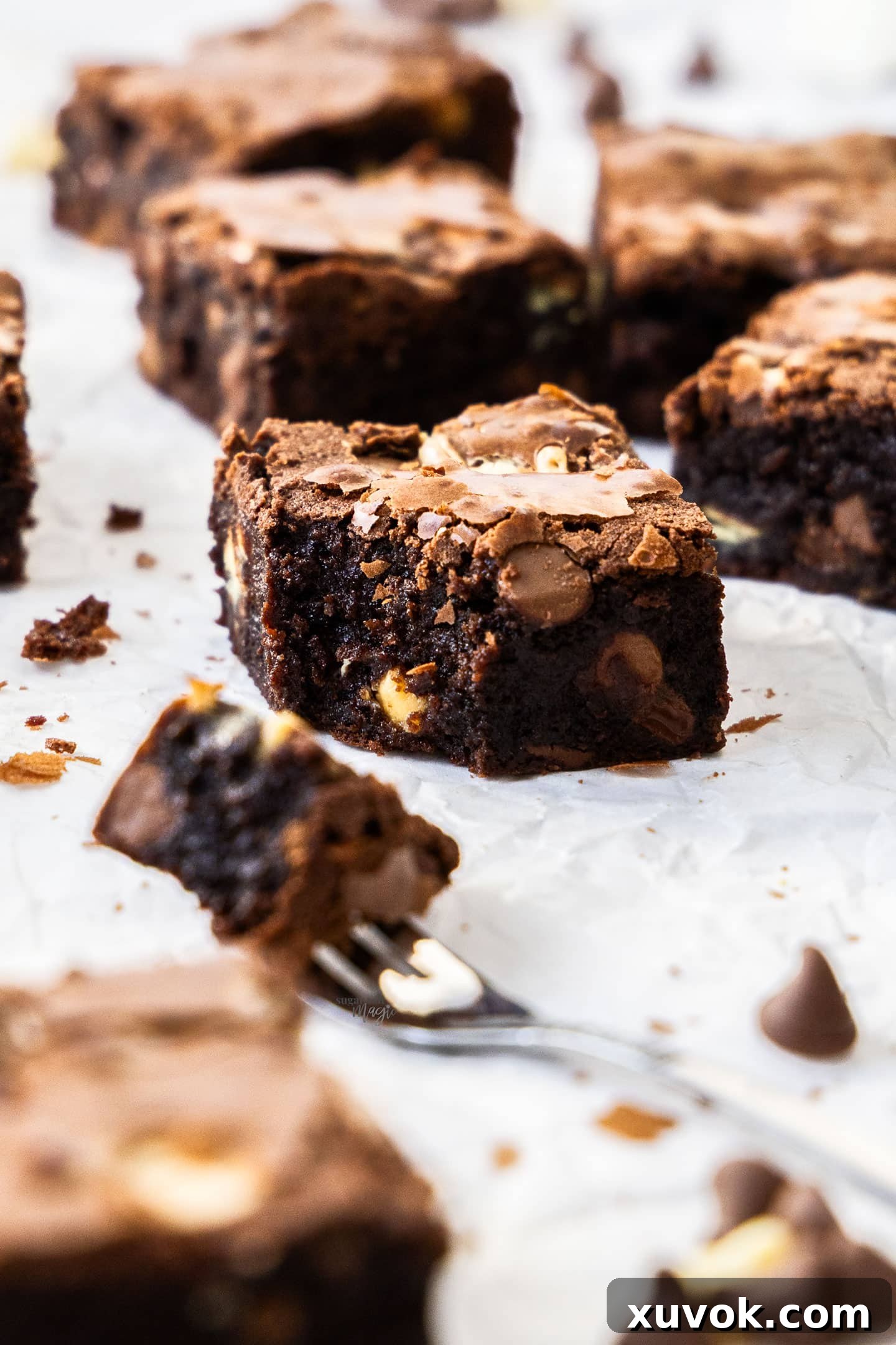 A perfectly cut triple chocolate brownie with a forkful removed, showing its dense, fudgy interior and visible chocolate chips.
