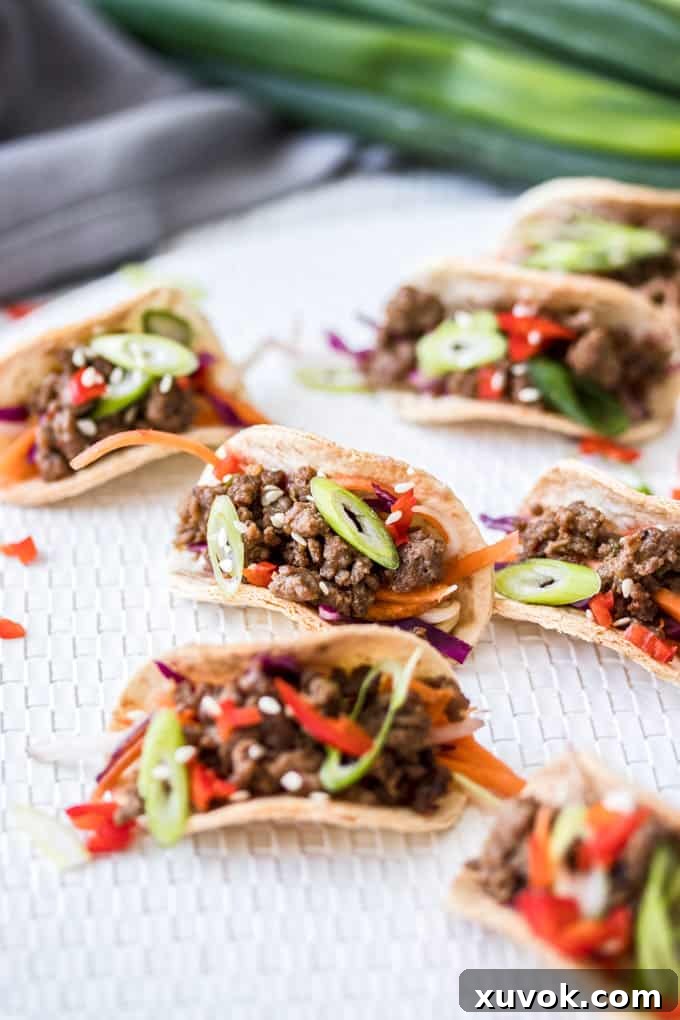 A group of mini tacos filled with ground beef bulgogi and Asian slaw on a white mat with green onions in the background. Ready to be served.