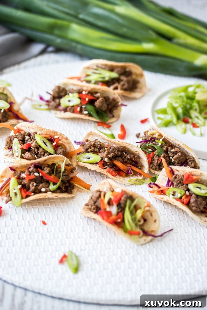 A group of mini Korean tacos on a white mat with a bunch of spring onions in the background. Ready to be served.