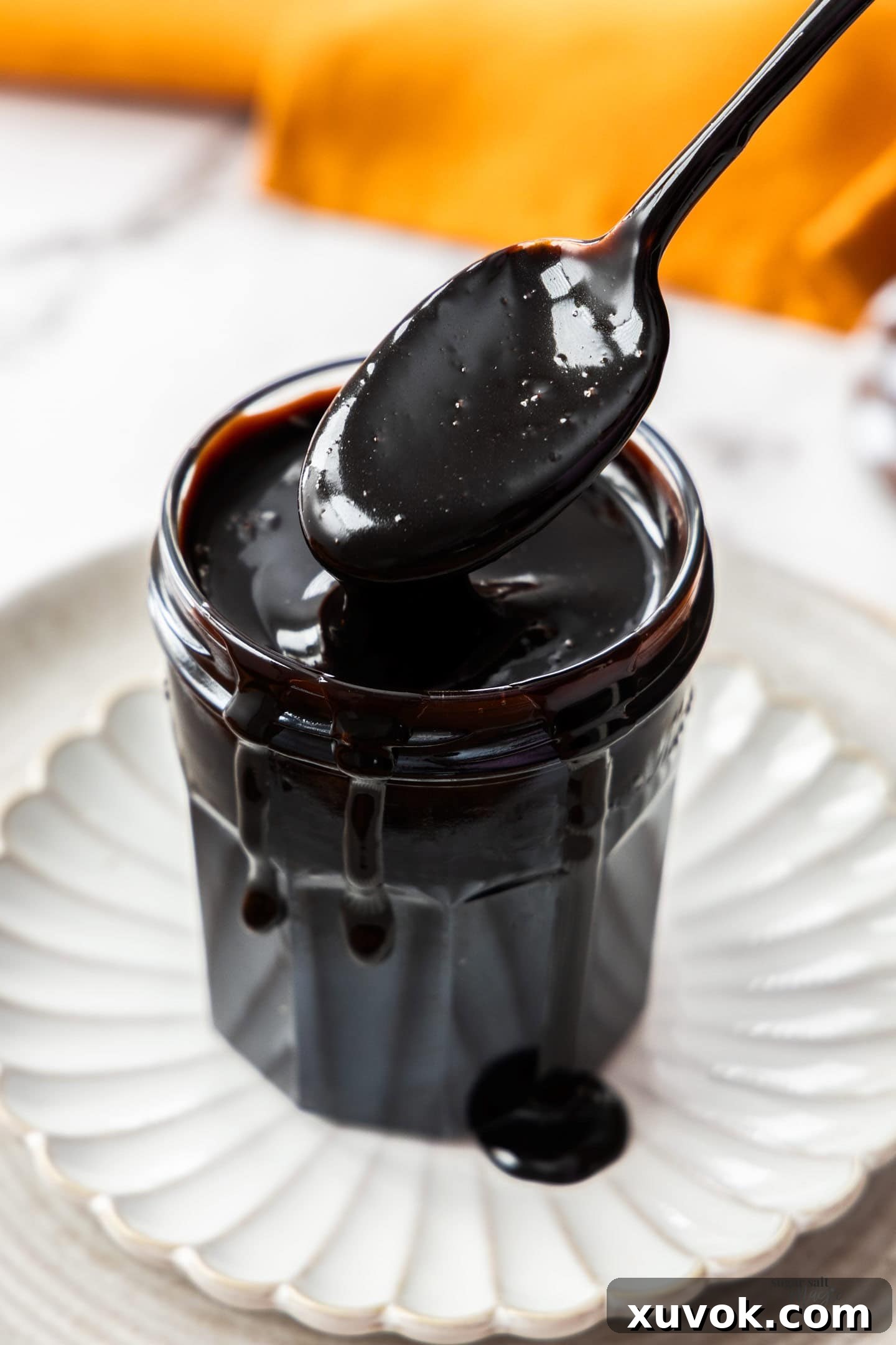 A spoon scooping some thick chocolate sauce out of a glass jar, showing its rich texture.