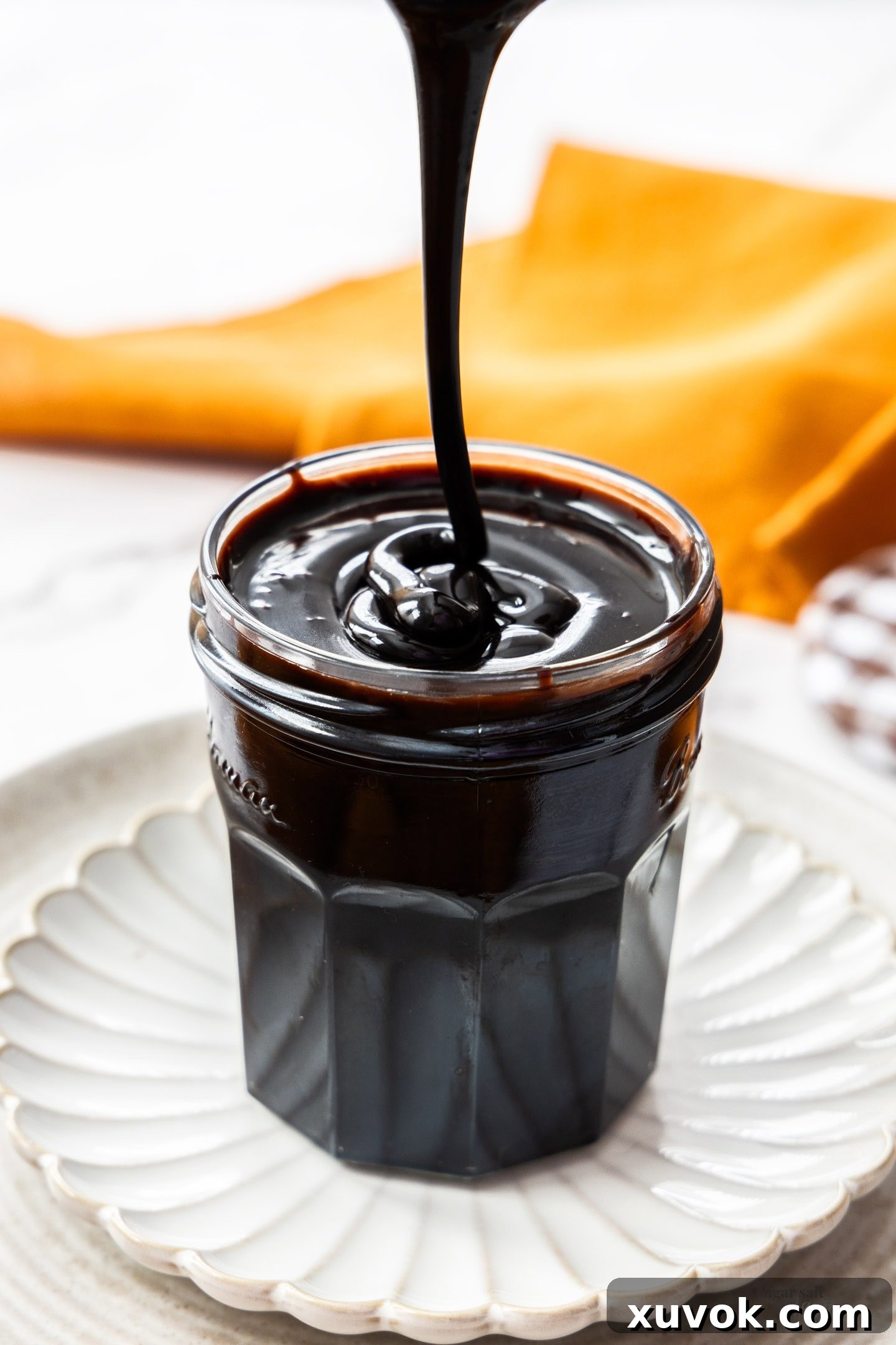 The finished chocolate sauce being poured and drizzled into a glass jar for storage.