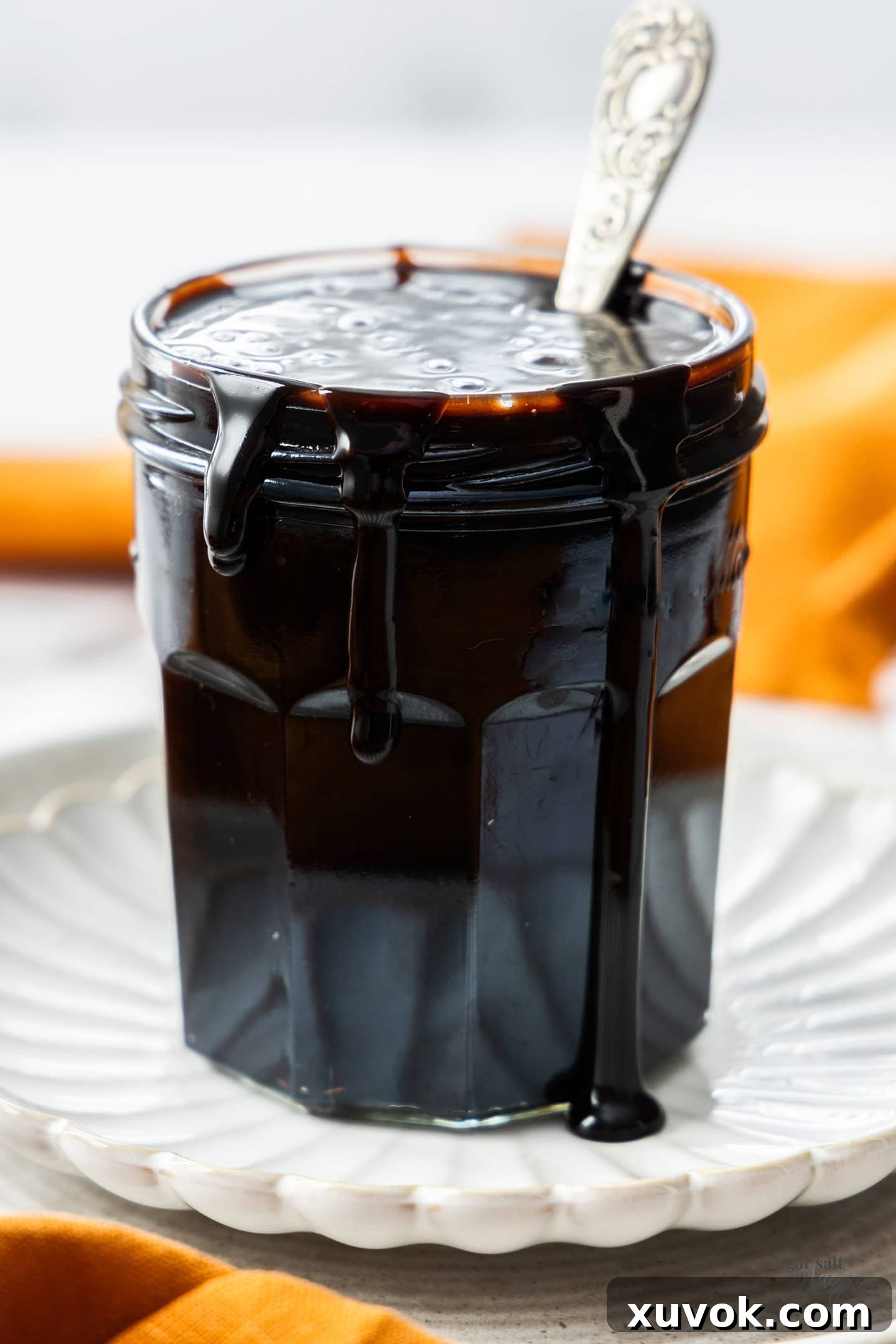 A glass jar of chocolate sauce with some sauce dripping down the sides, indicating its rich texture.