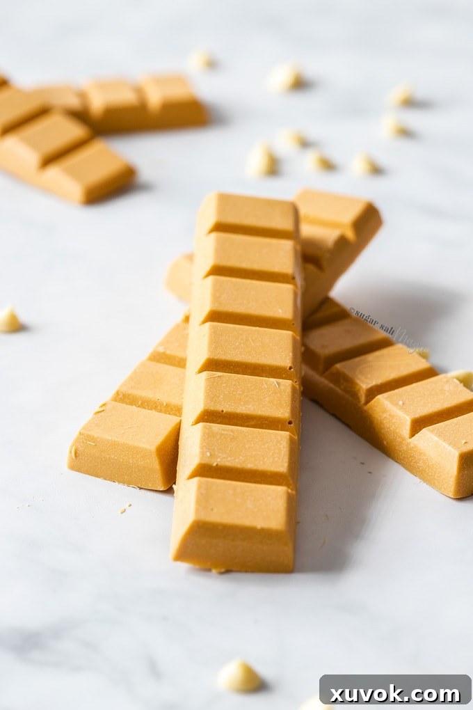 Bars of caramelised white chocolate on a marble surface, surrounded by white chocolate chips, styled for presentation.