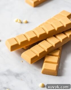 A stack of blocks of caramelised white chocolate with white chocolate chips scattered around them, on a marble surface.