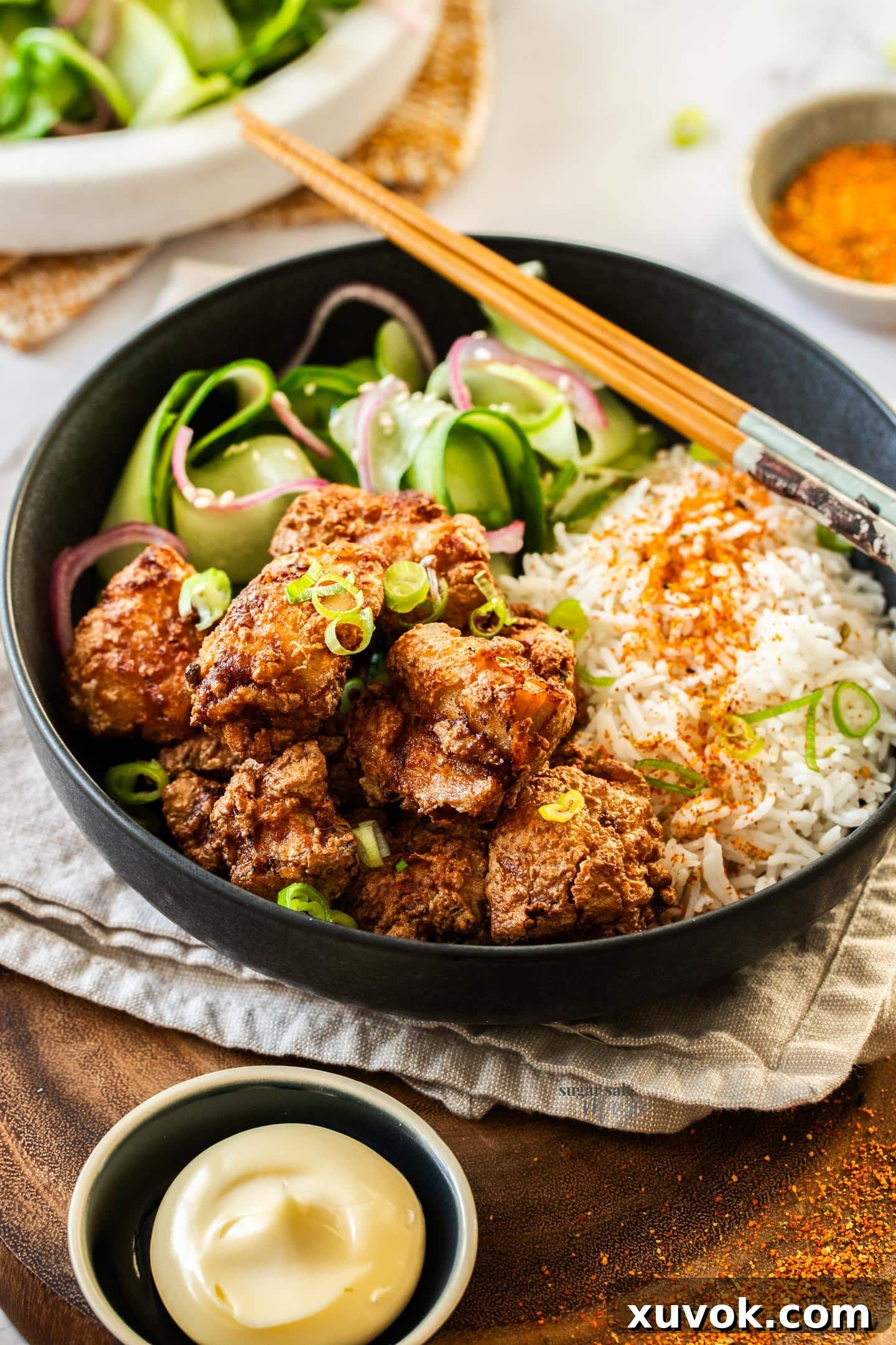 A bowl of golden-brown Karaage chicken, served with fluffy white rice and fresh cucumber slices, with a small pot of Kewpie mayonnaise in the foreground.