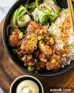 A black bowl filled with perfectly fried Karaage Chicken pieces atop fluffy white rice, garnished for a delicious meal.