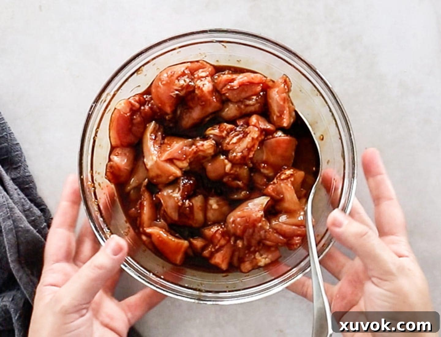Bite-sized chunks of raw chicken thigh marinating in a savory, light brown sauce within a glass bowl.