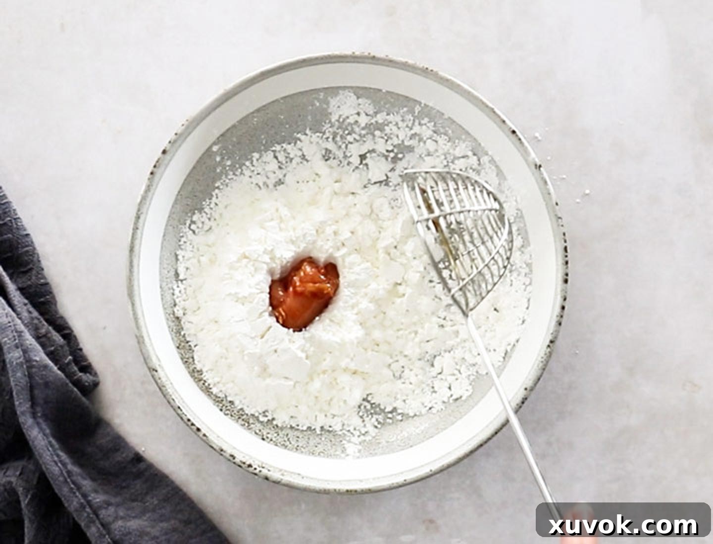 A piece of marinated chicken thigh being coated in white potato starch in a shallow bowl, ready for frying.