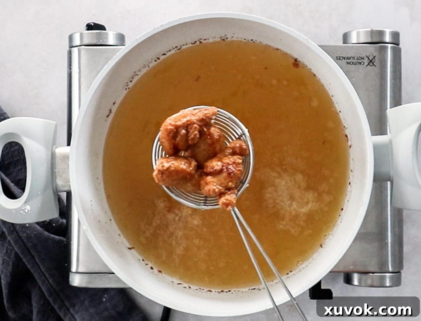A wire spider strainer carefully lifting perfectly golden and crispy Japanese fried chicken pieces from a pan of hot oil.