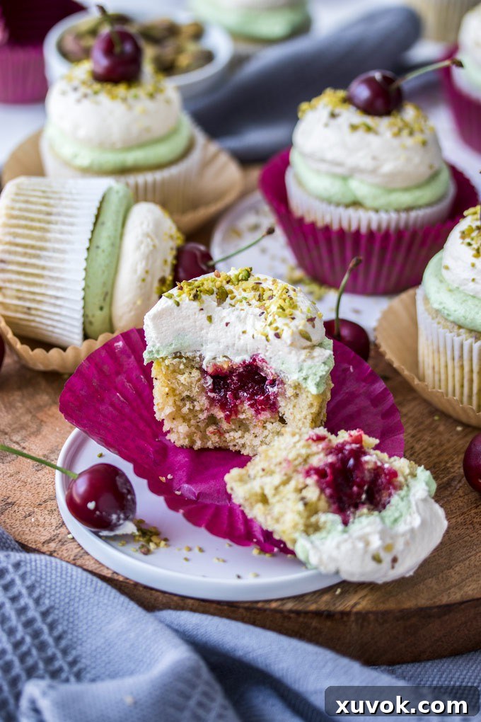 A Cherry Pistachio Cupcake cut open to reveal the bright red cherry compote filling inside, showcasing its delicious layers.
