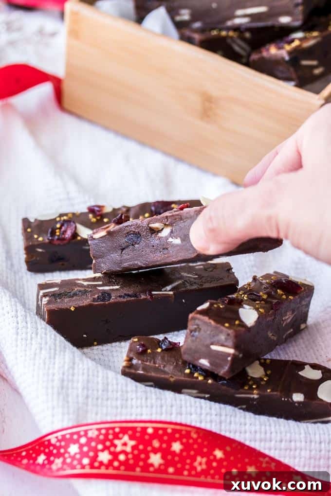 A hand picking up a slice of Christmas Fudge from a pile.