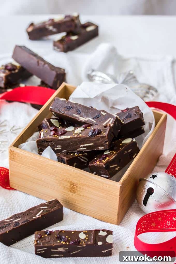 A wooden box filled with Christmas Fudge next to a silver bell and red ribbon.