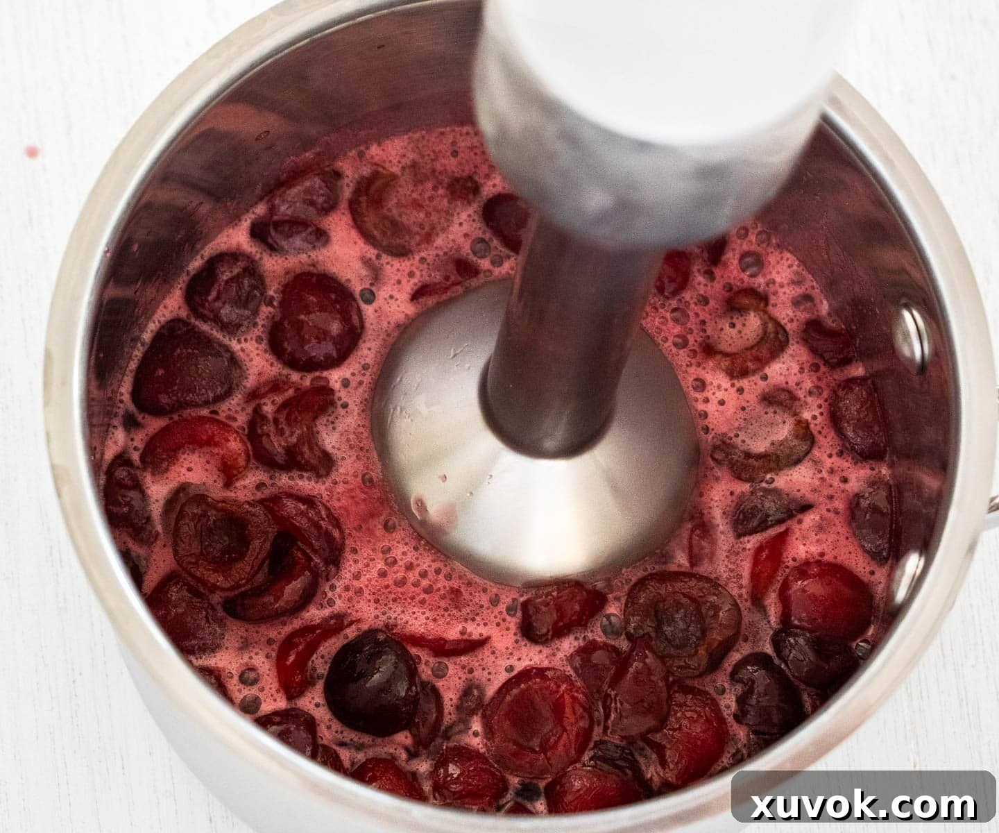 Blending the cherry sauce with an immersion blender.