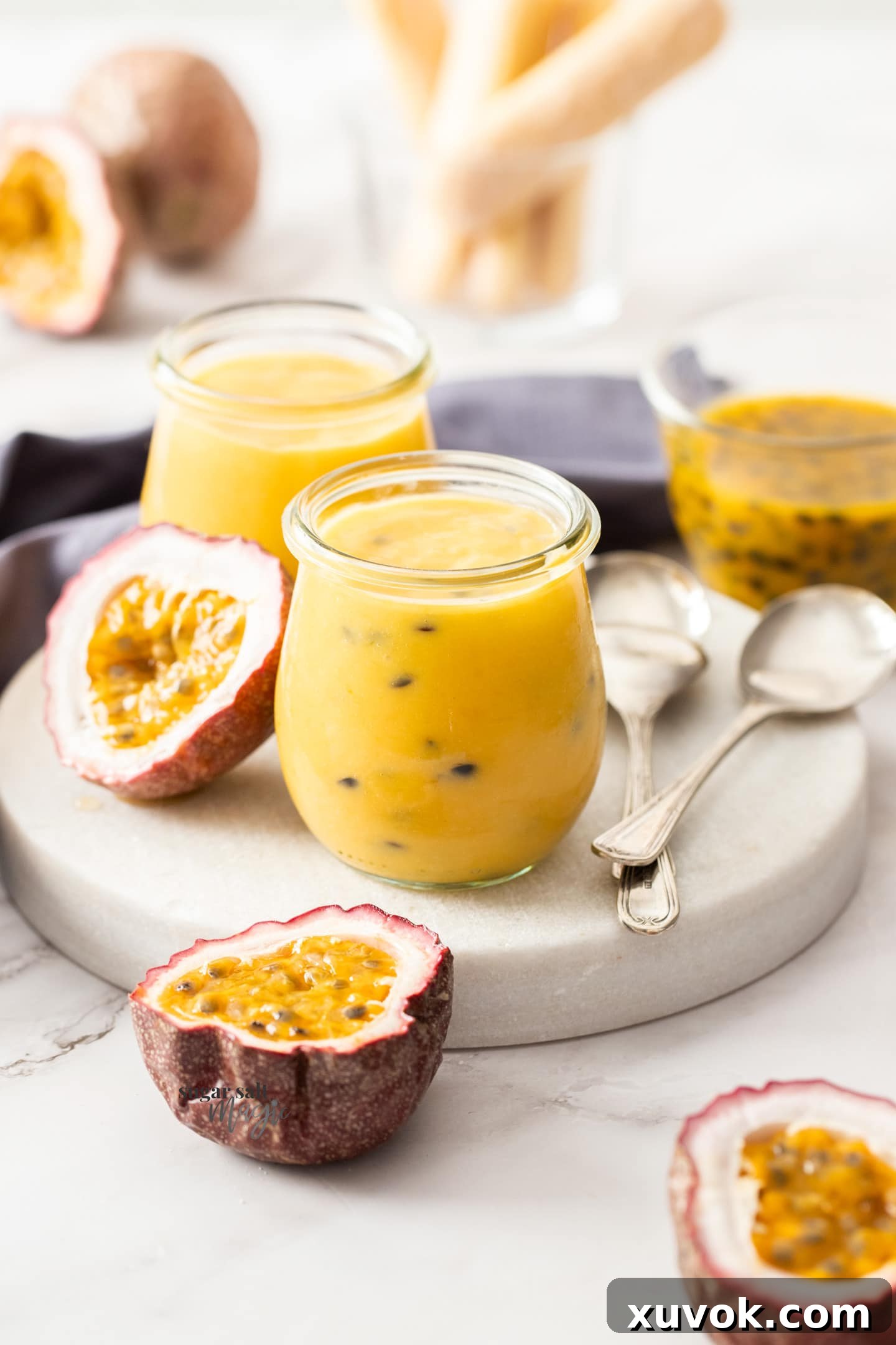 Two small glass jars of vibrant passionfruit curd displayed elegantly on a pristine white marble platter, highlighting its rich golden hue.