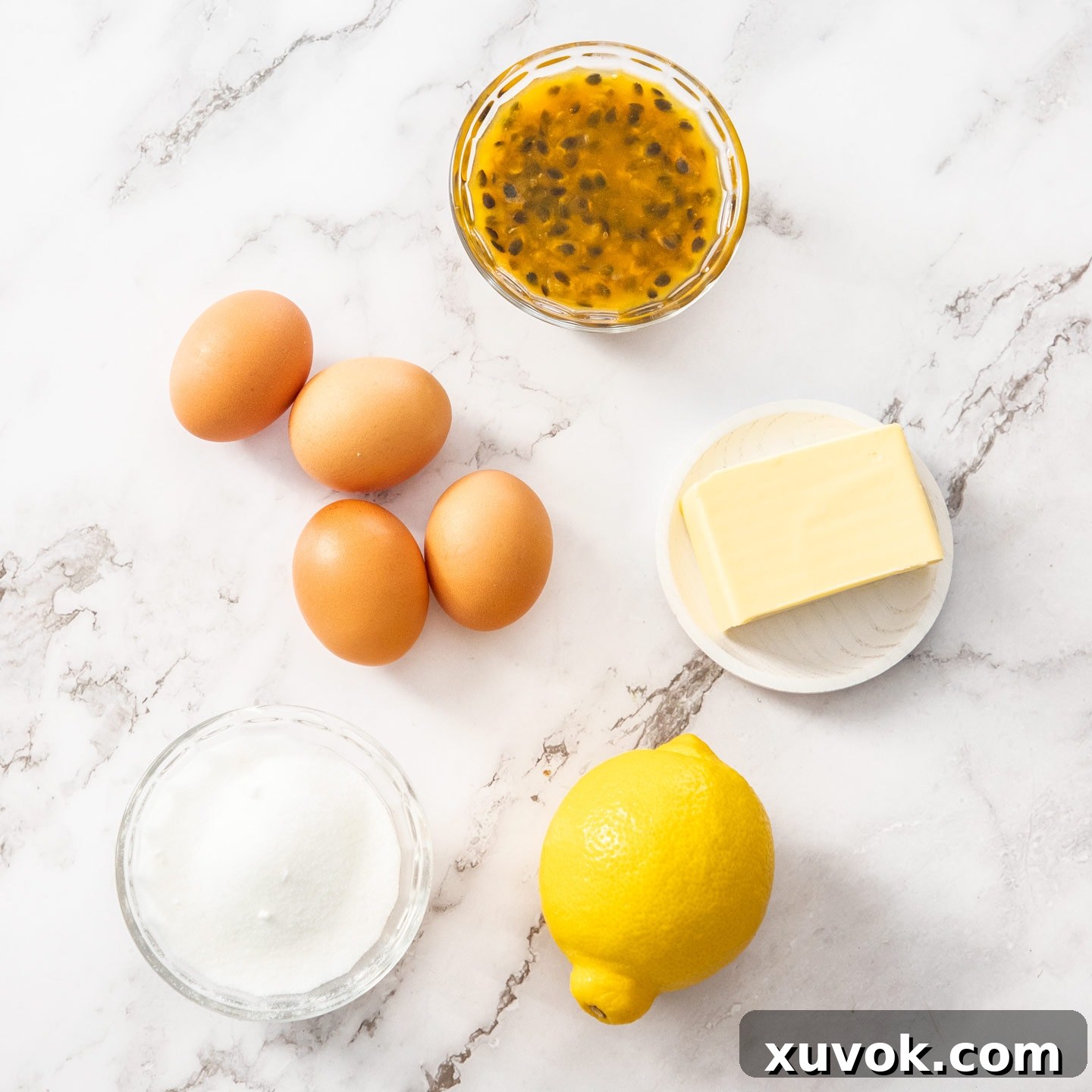 The five essential ingredients for making passionfruit curd artfully arranged on a clean marble surface.