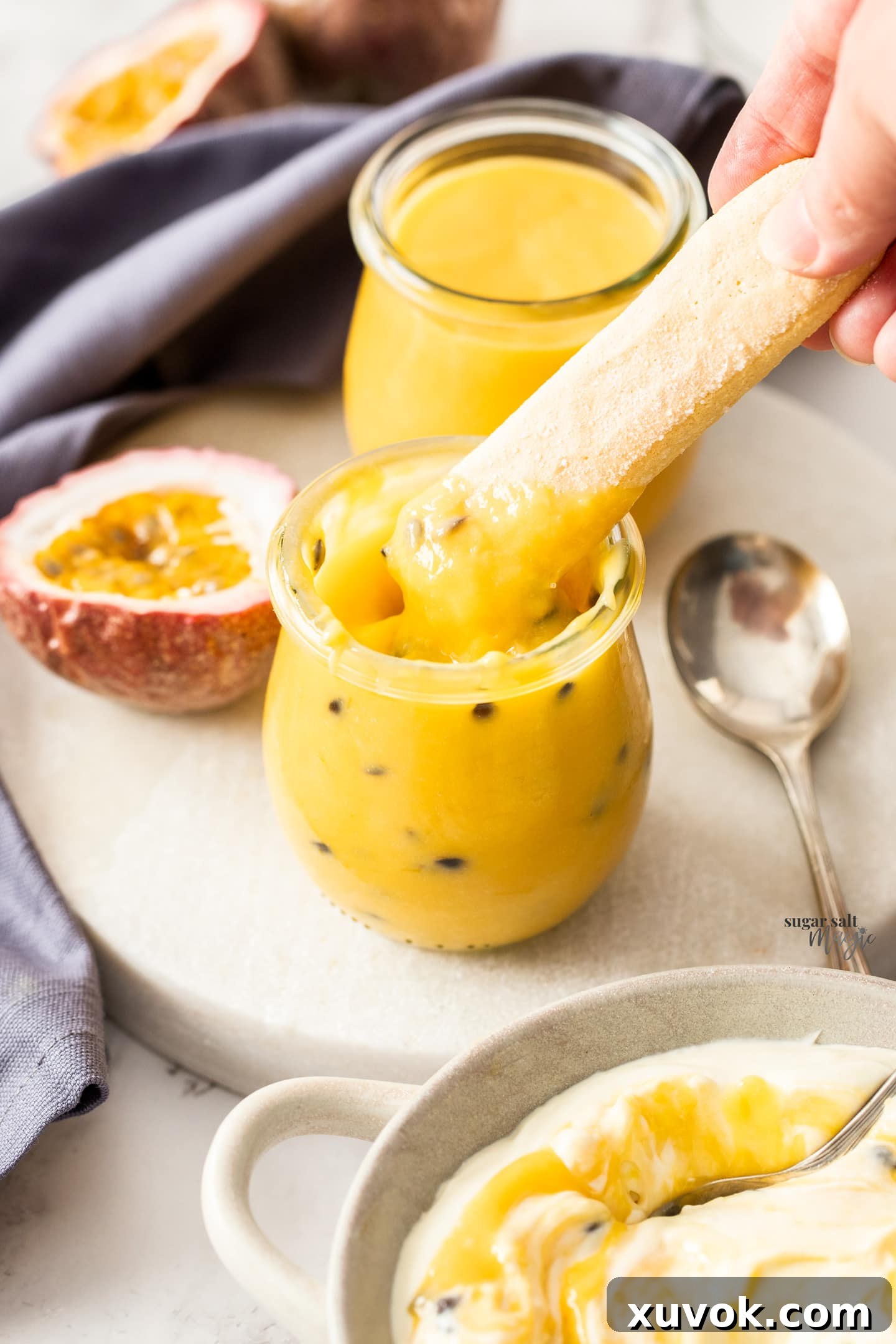 A delicate sponge finger biscuit being dipped into a small jar of vibrant homemade passionfruit curd.