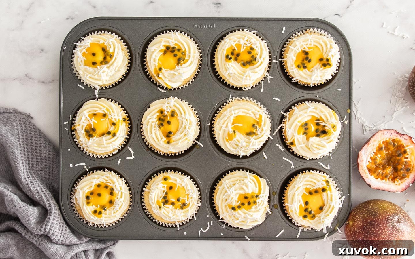The finished passionfruit cupcakes arranged in a muffin pan, beautifully decorated with coconut buttercream, shredded coconut, and a drizzle of passionfruit pulp.