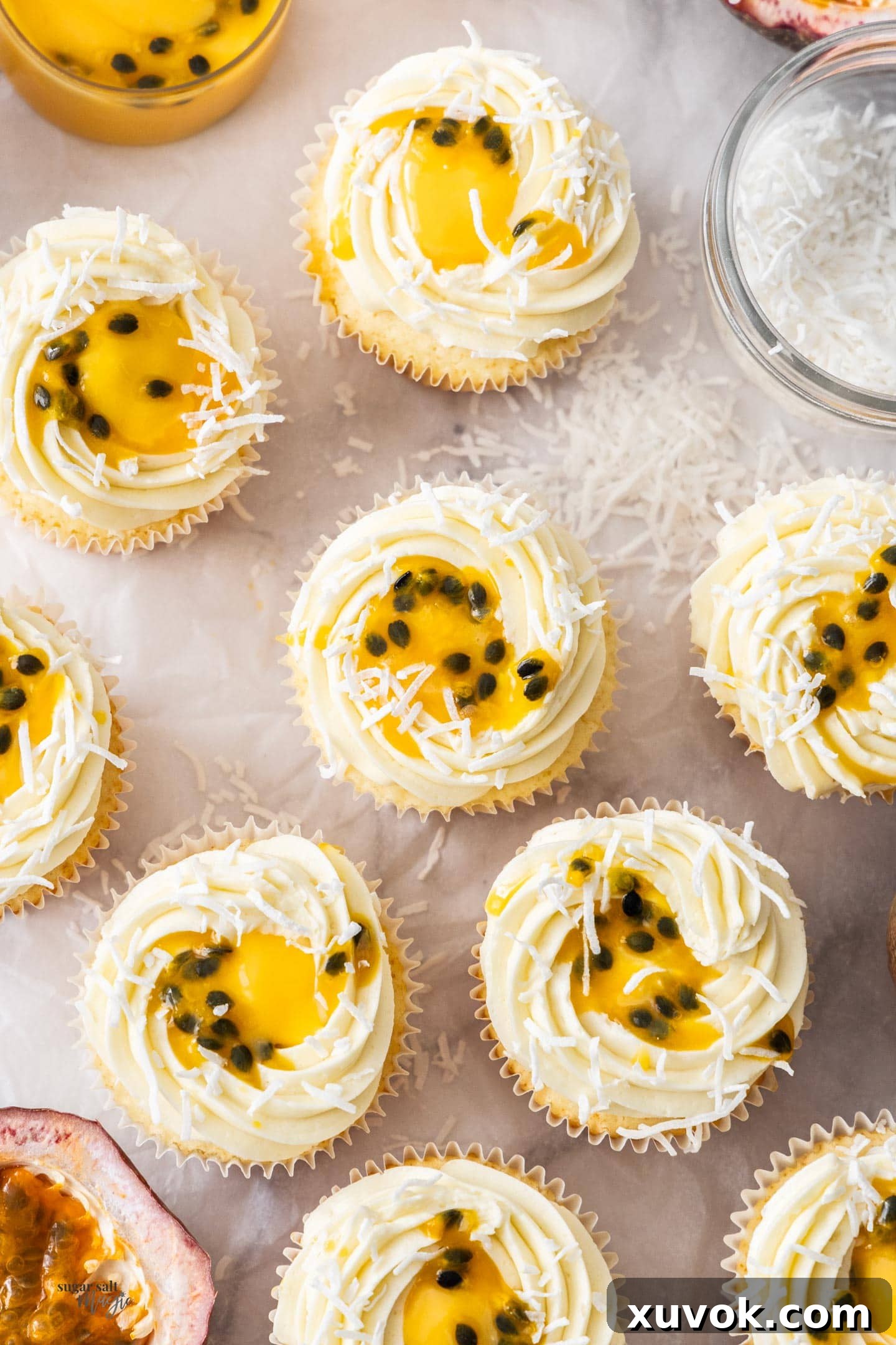 Top-down view of several passionfruit cupcakes, showing the intricate piping of the coconut buttercream, fresh passionfruit seeds, and shredded coconut.