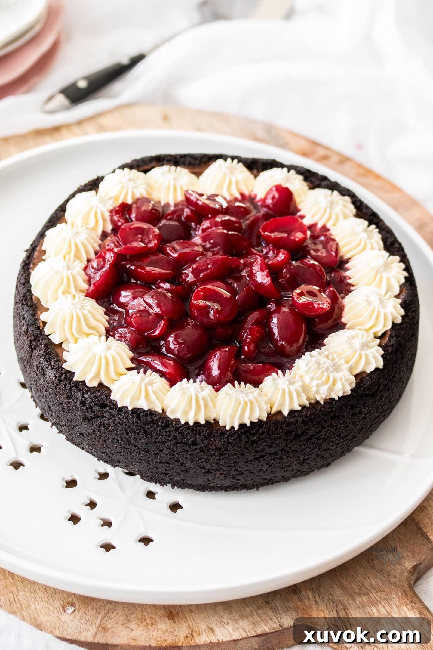 A whole black forest cheesecake on a platter, showcasing its dark chocolate crust, creamy filling, and luscious cherry topping with whipped cream rosettes.