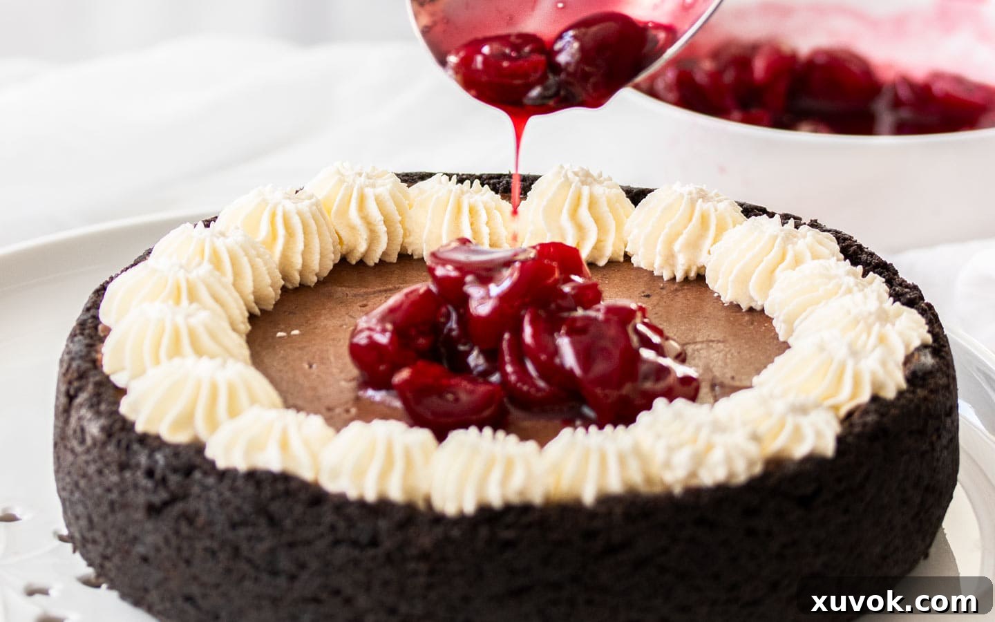 Luscious cherry sauce being poured gracefully into the center of the decorated Black Forest Cheesecake.