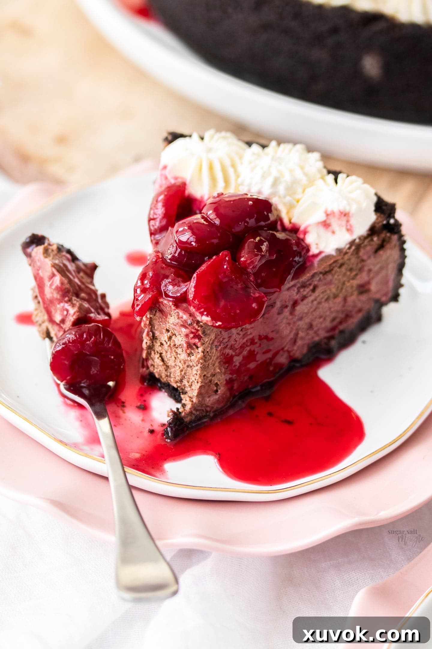 A fork taking a scoop from a slice of Black Forest Cheesecake, revealing its creamy texture and the rich Oreo crust.
