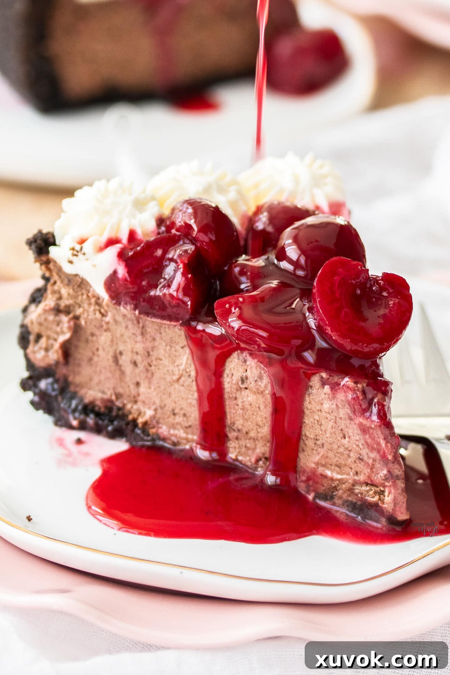 A tempting slice of black forest cheesecake on a plate, with glossy cherry sauce being drizzled over it.