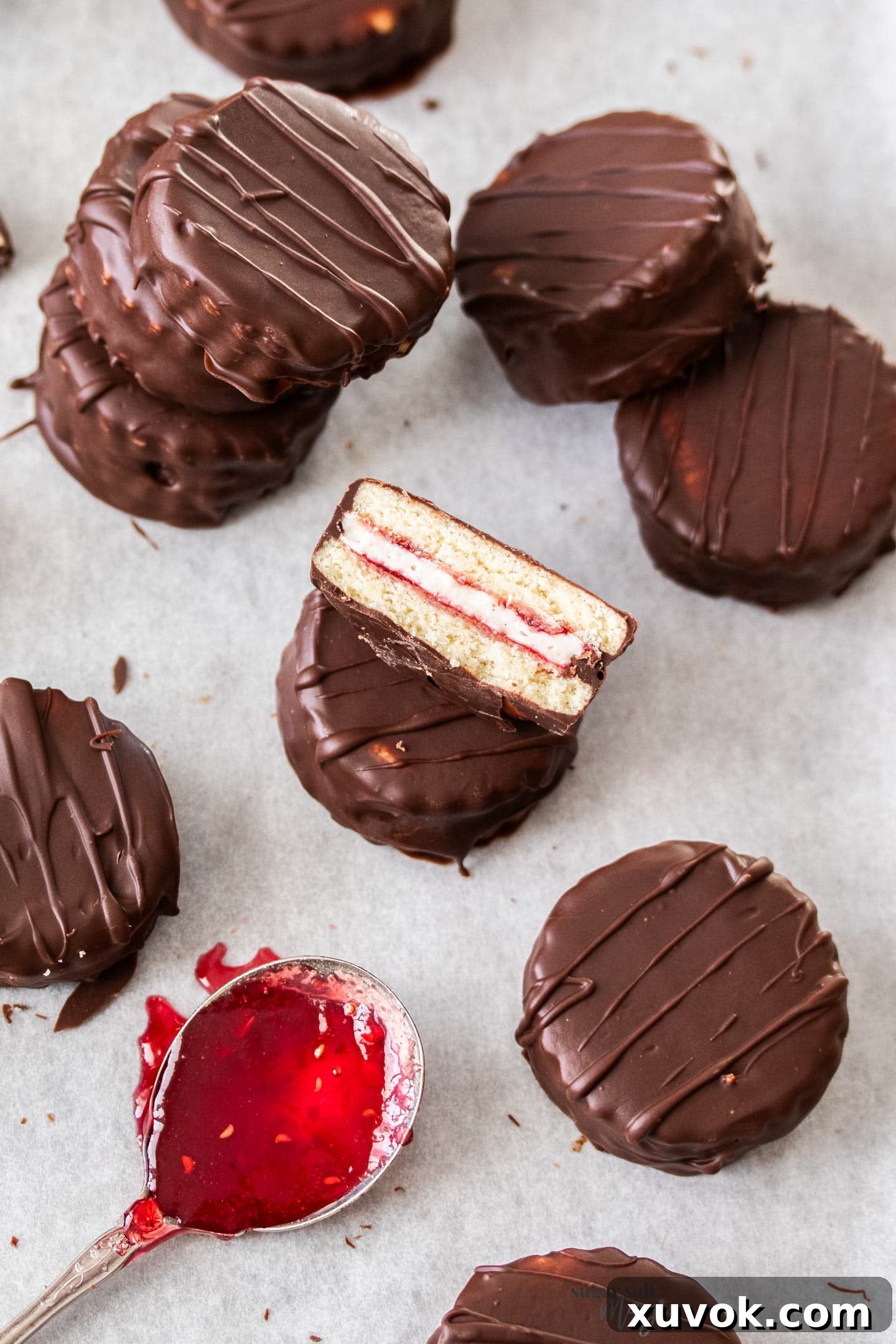 Top down view of a batch of mini homemade wagon wheels with one cut in half, showcasing layers of cookie, marshmallow, jam, and chocolate.