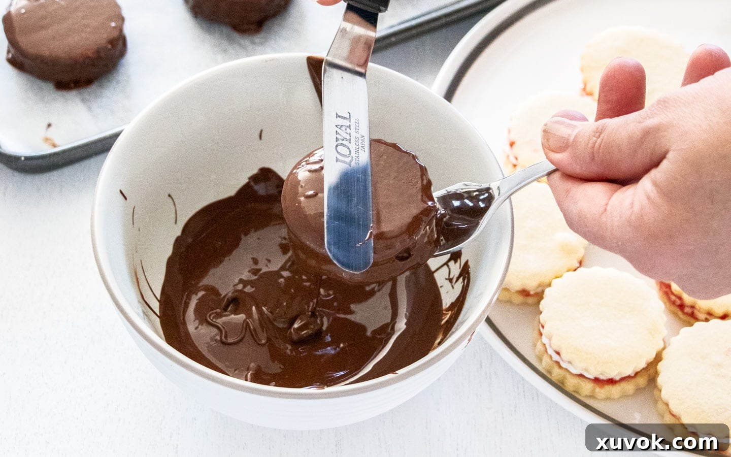 Using a spatula to scrape away excess chocolate from a coated wagon wheel.