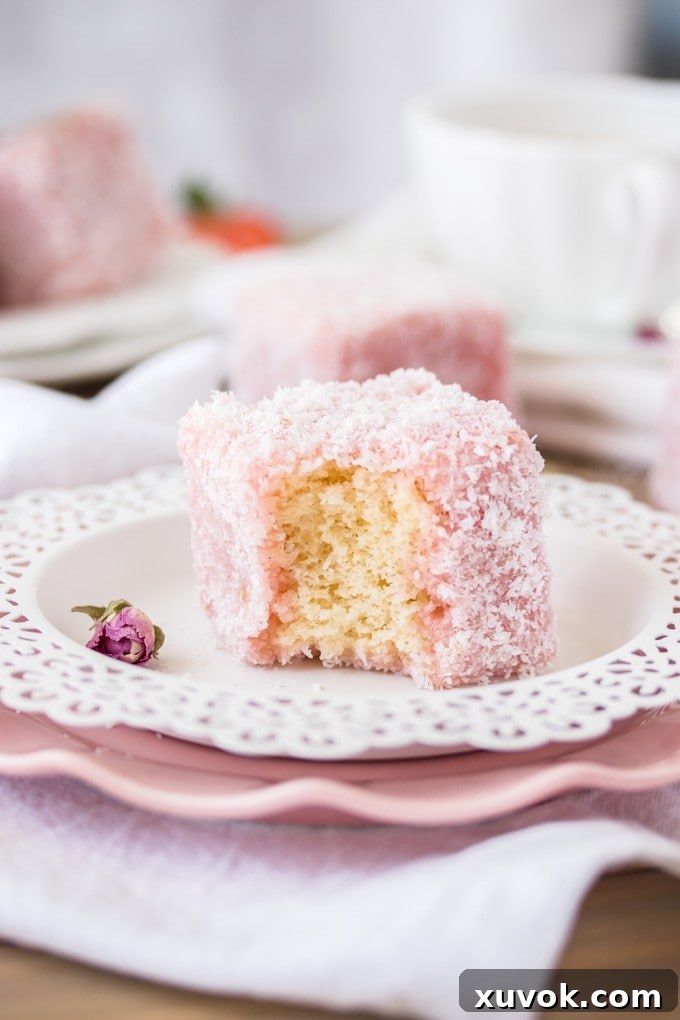 A half eaten Rose Strawberry Lamington on a plate next to a dry rose