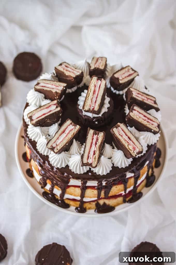 A beautifully assembled Wagon Wheel Cake on a pristine cake stand, surrounded by scattered mini Wagon Wheels on a white surface. The multi-layered cake is adorned with a smooth chocolate ganache and decorative marshmallow frosting swirls, creating an inviting dessert scene.