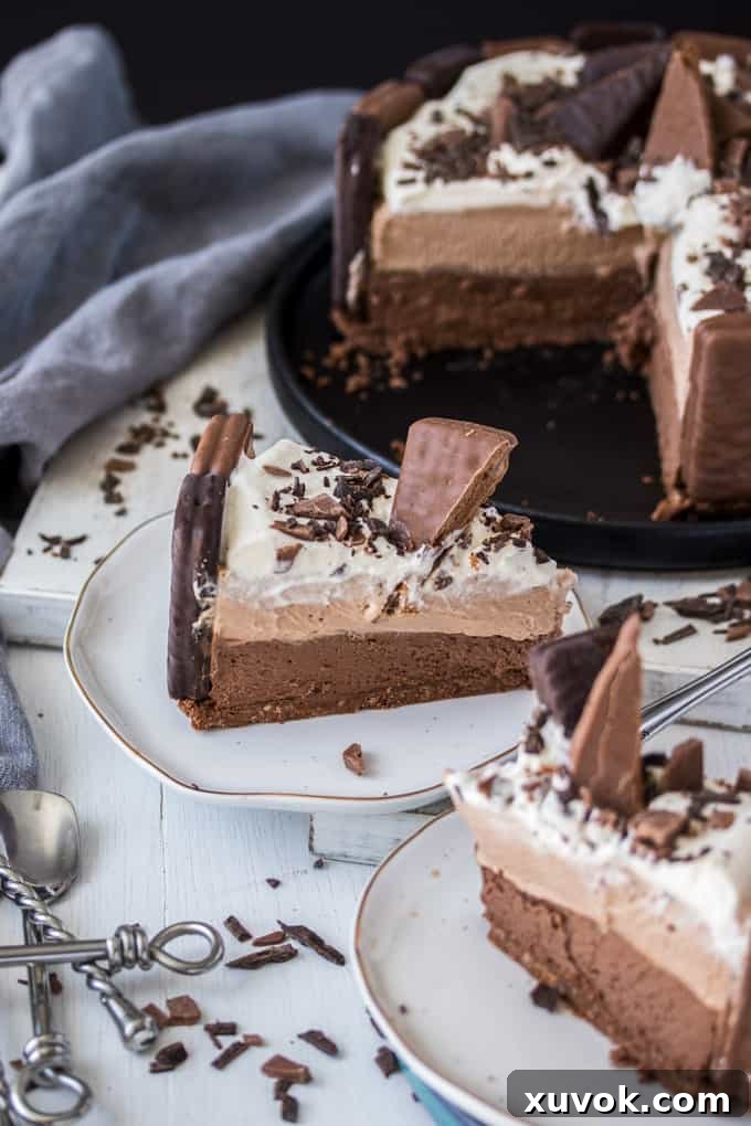 2 slices of No Bake Tim Tam Cheesecake on white plates, the whole cheesecake is in the background
