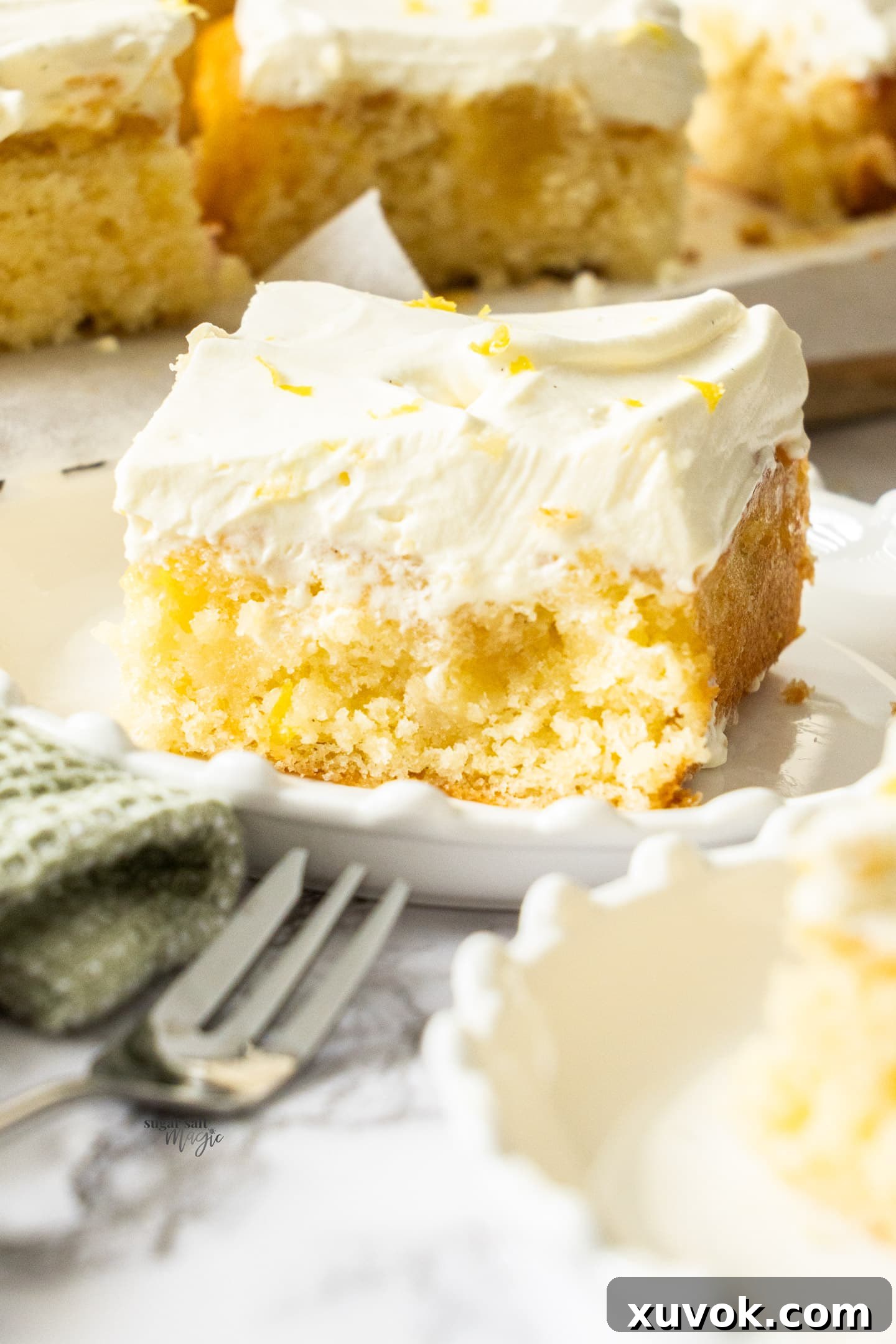 A moist slice of lemon poke cake on a dessert plate, showing the infused lemon syrup.