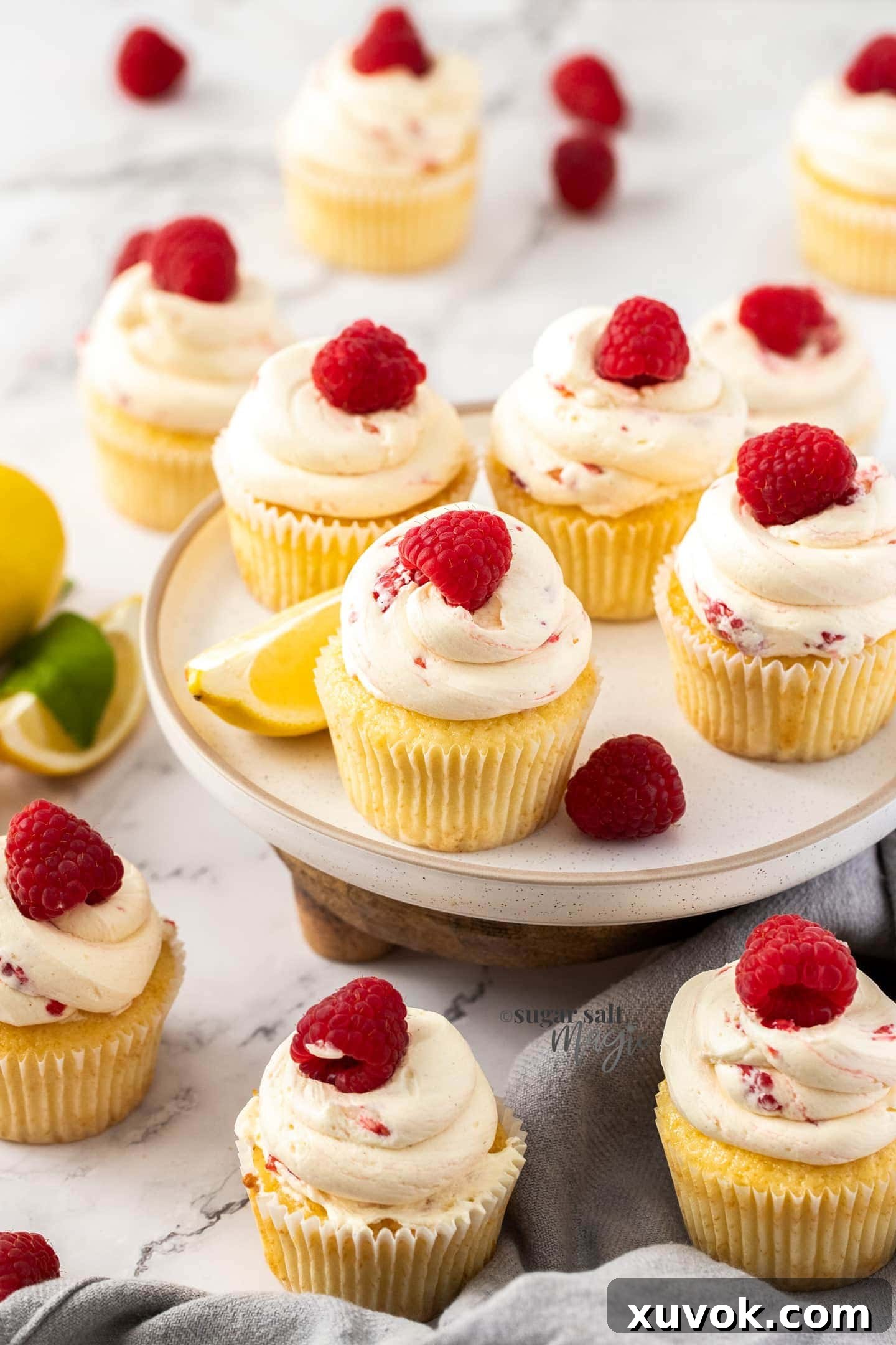 A batch of fluffy lemon raspberry cupcakes topped with fresh raspberries on a white plate.