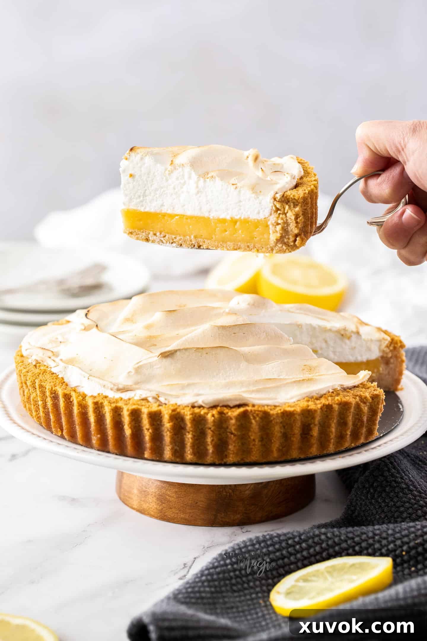 A slice of lemon meringue pie being held above the rest of the pie, showcasing the layers.