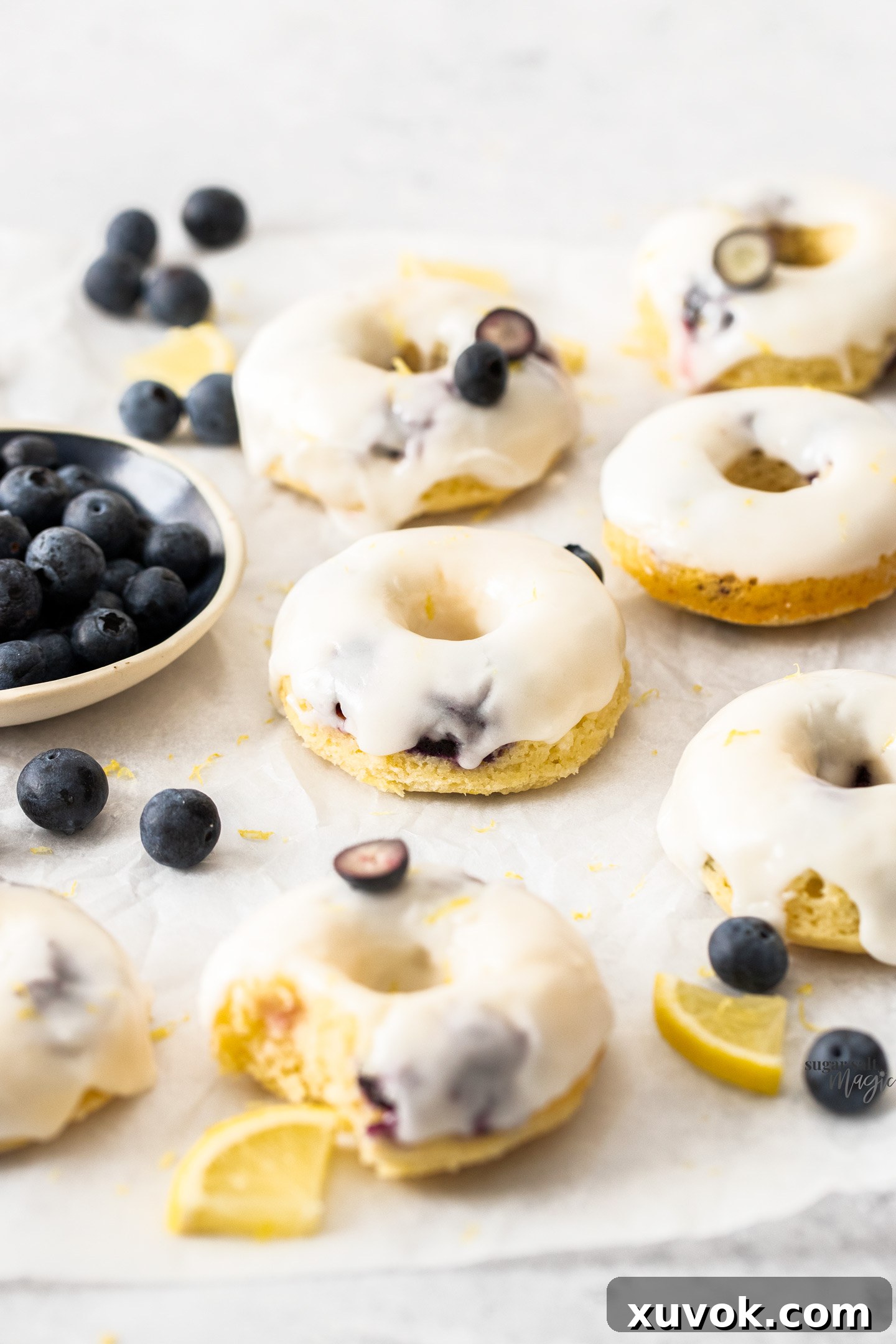 A batch of delicious iced blueberry cake donuts on a sheet of baking paper.